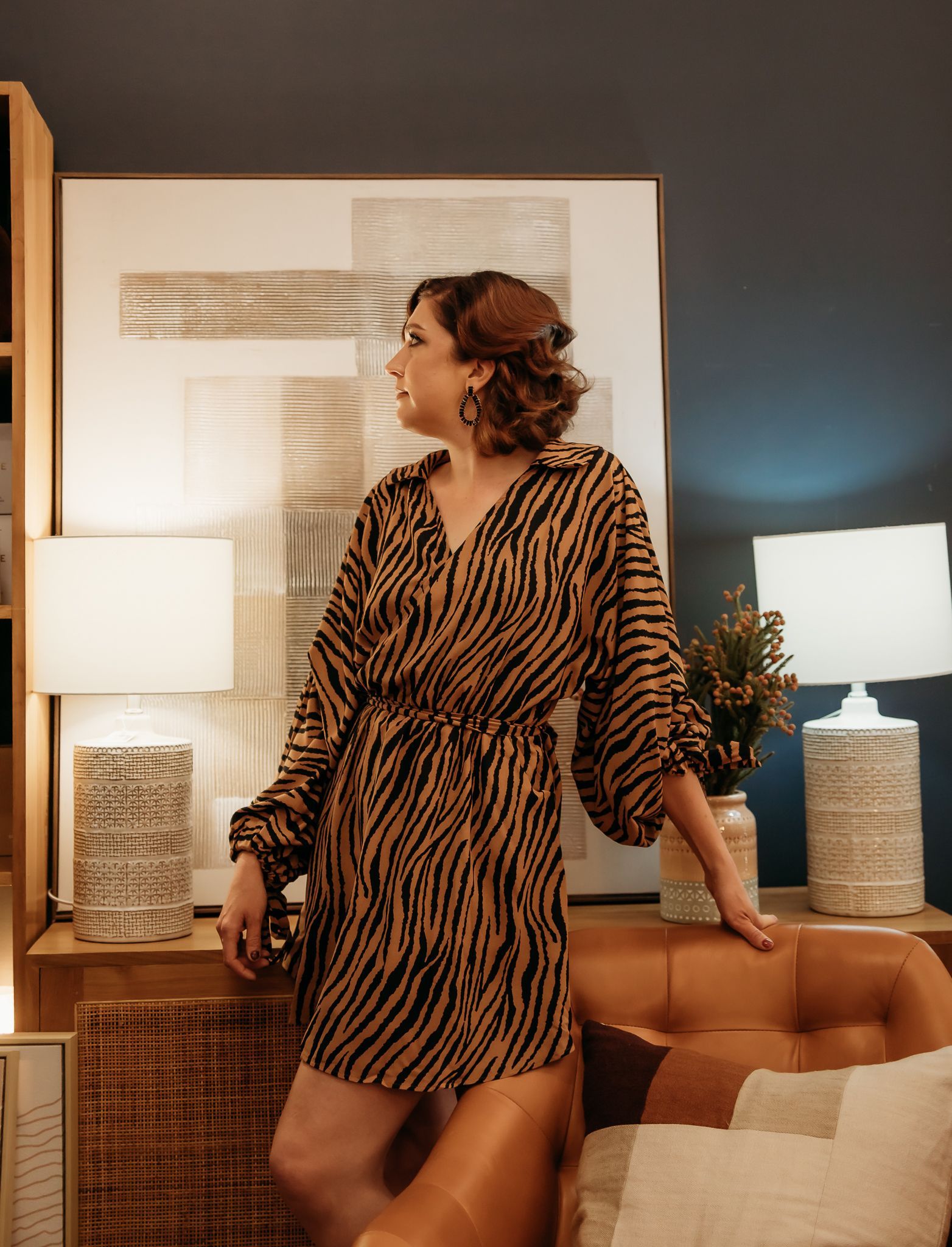 A woman in a zebra print dress is standing next to a couch in a living room — Lavie Hair & Beauty in Ciccone, NT
