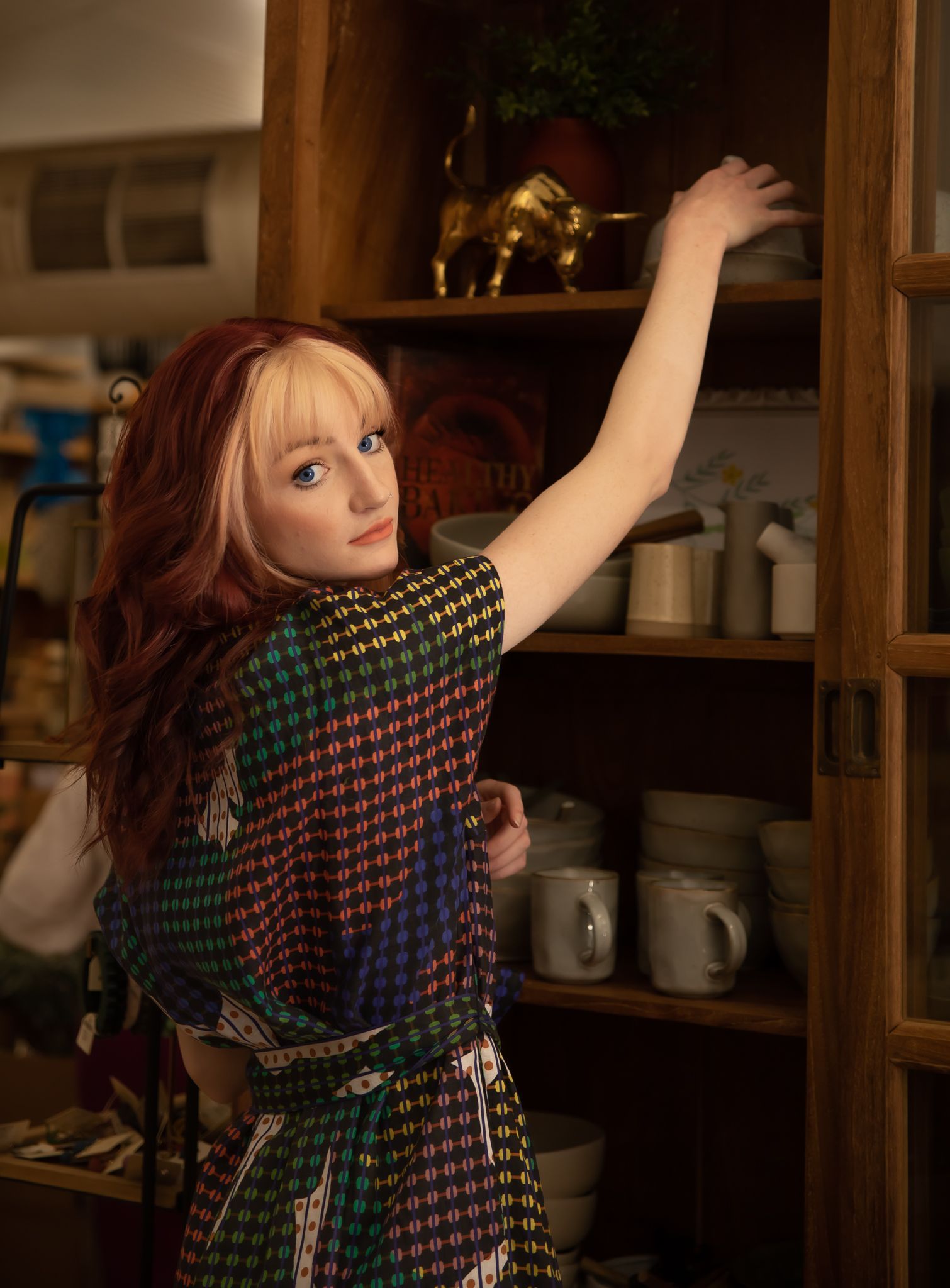 A woman in a colourful dress is reaching for something on a shelf — Lavie Hair & Beauty in Ciccone, NT