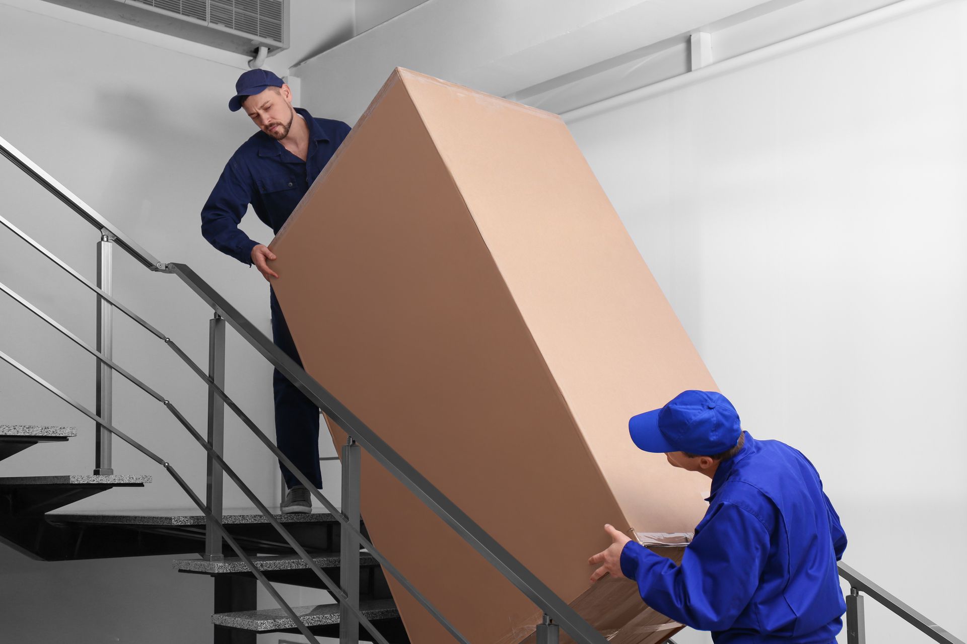 Professional workers carrying refrigerator on stairs indoors.