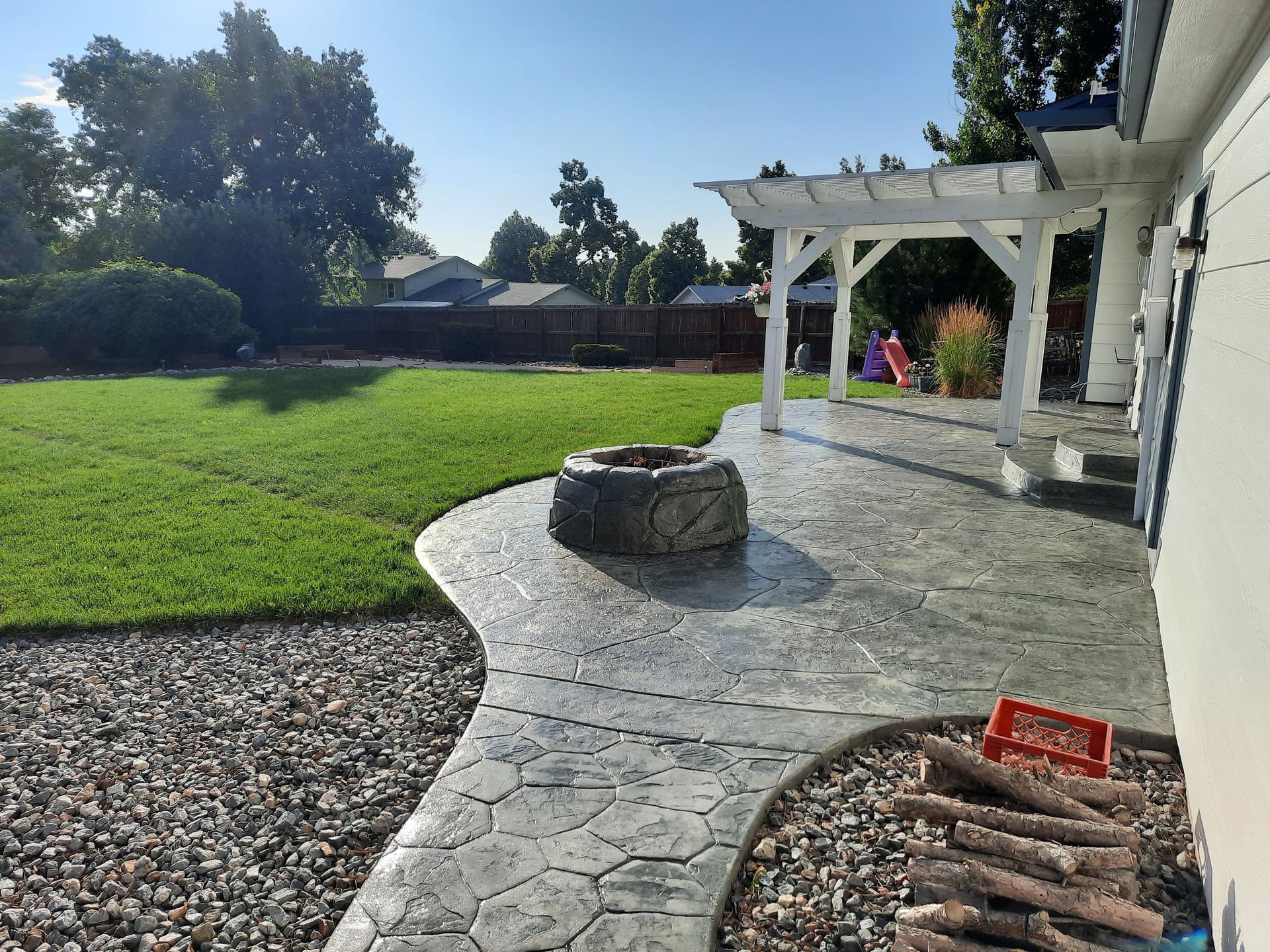 A patio with a fire pit and a pergola in the backyard