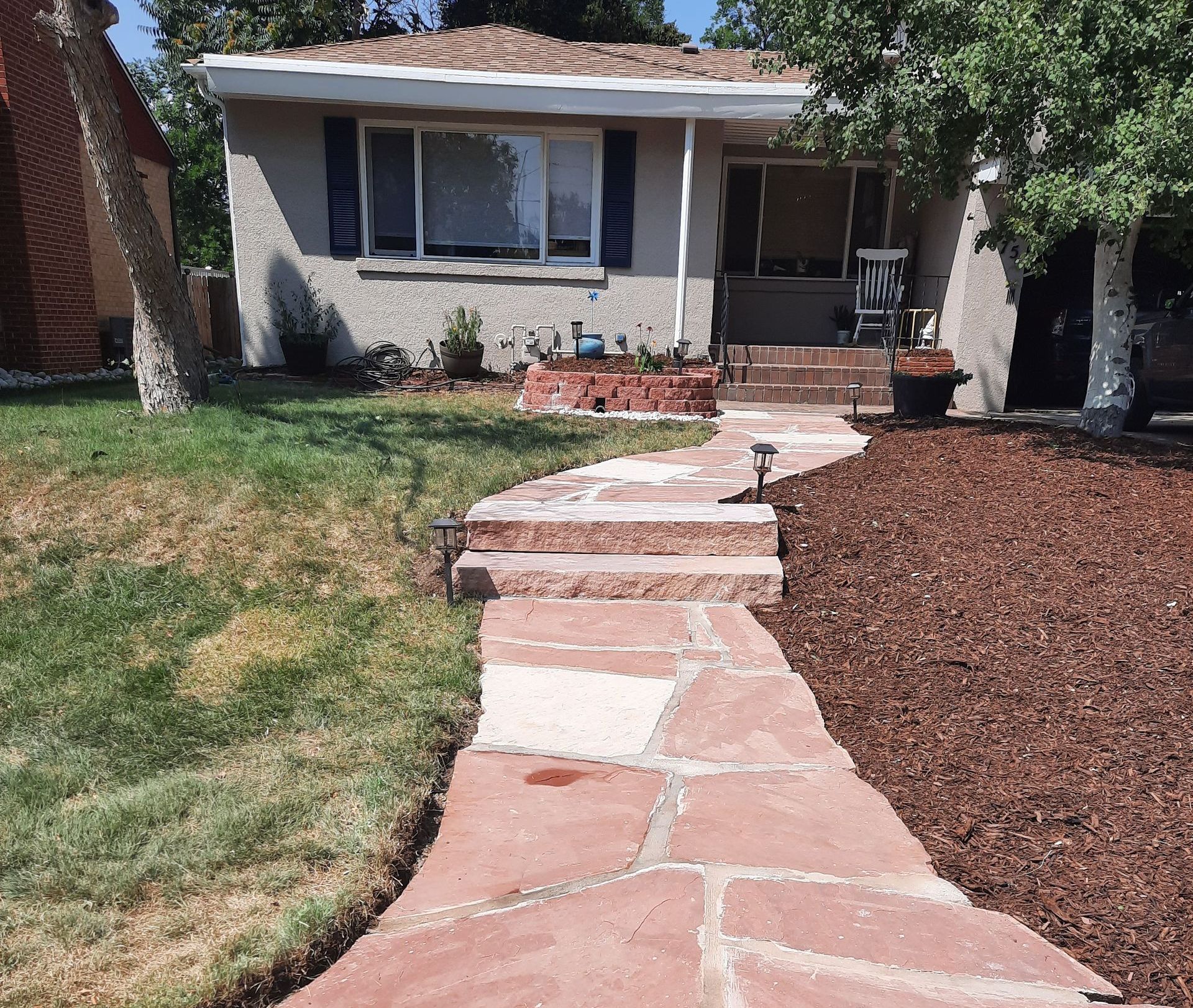 A stone walkway leading to a house with steps and mulch.