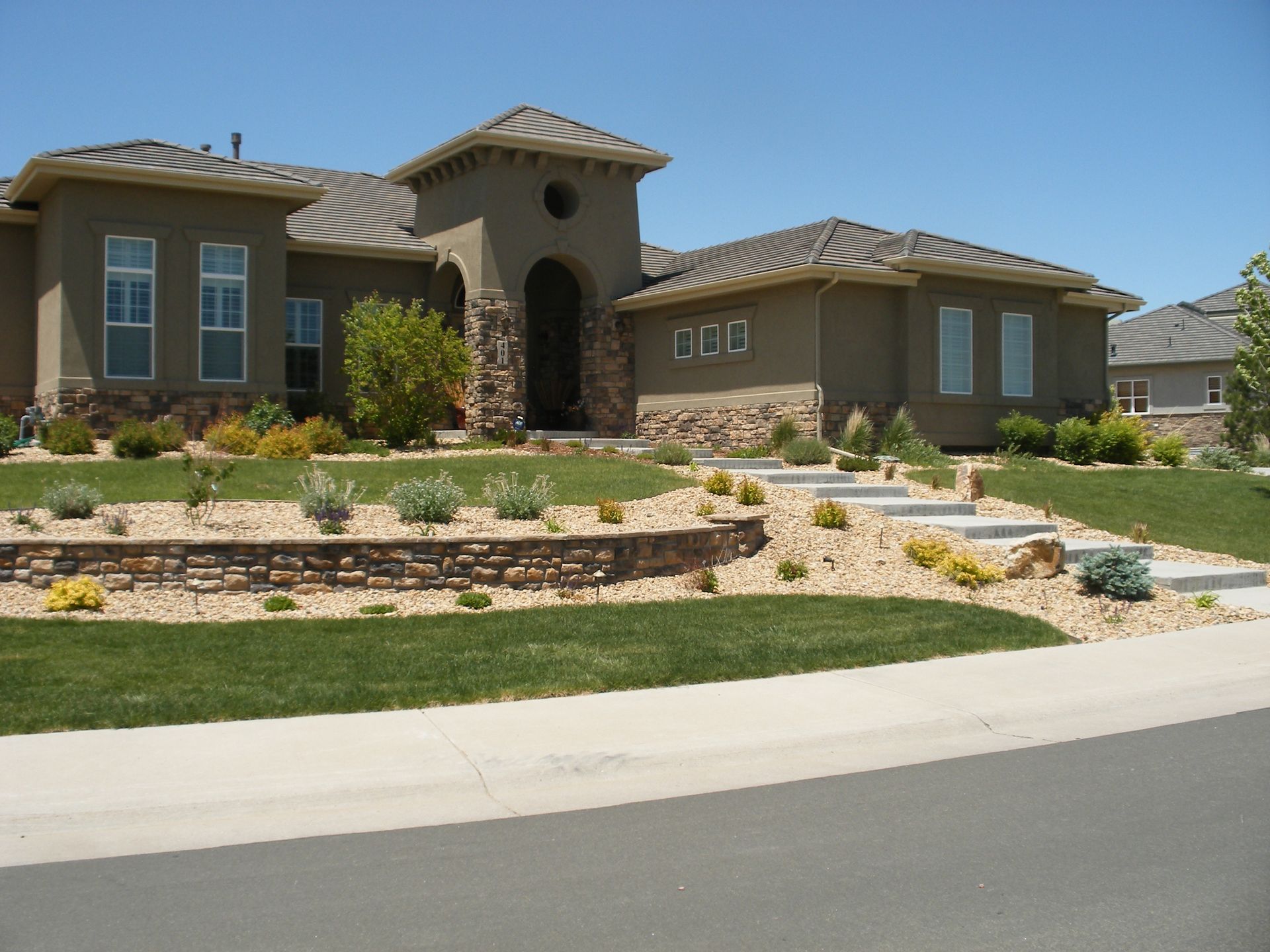 House with stucco exterior, stone accents, landscaped front yard, and a blue sky.