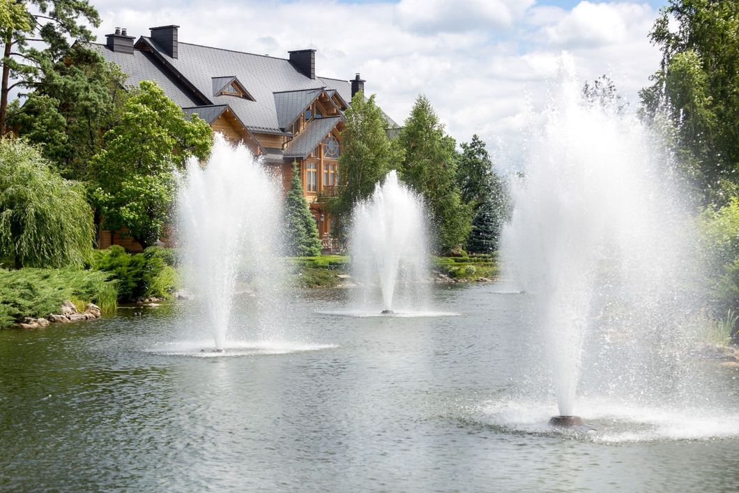 A fountain in a lake with a house in the background