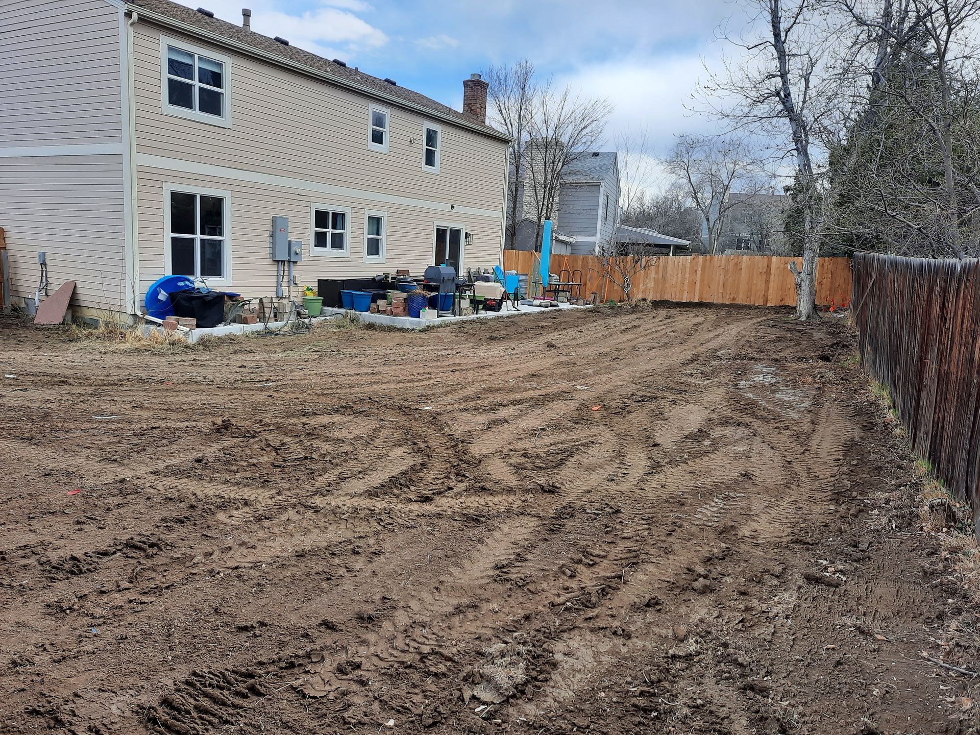 A large dirt field in front of a house with a wooden fence.