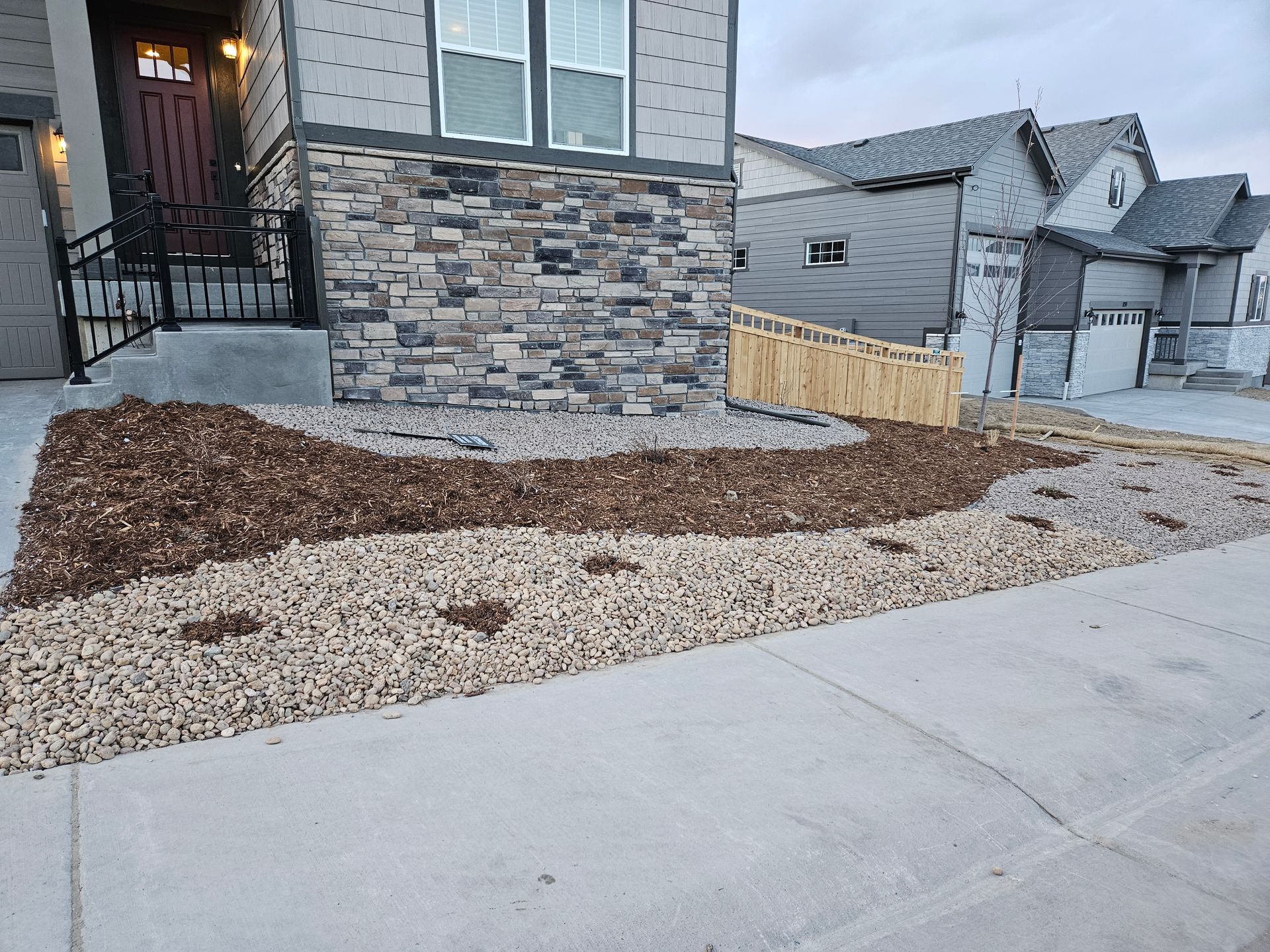 Gravel landscaping with small patches of soil for planting in front of a garage and adjacent to a fence.