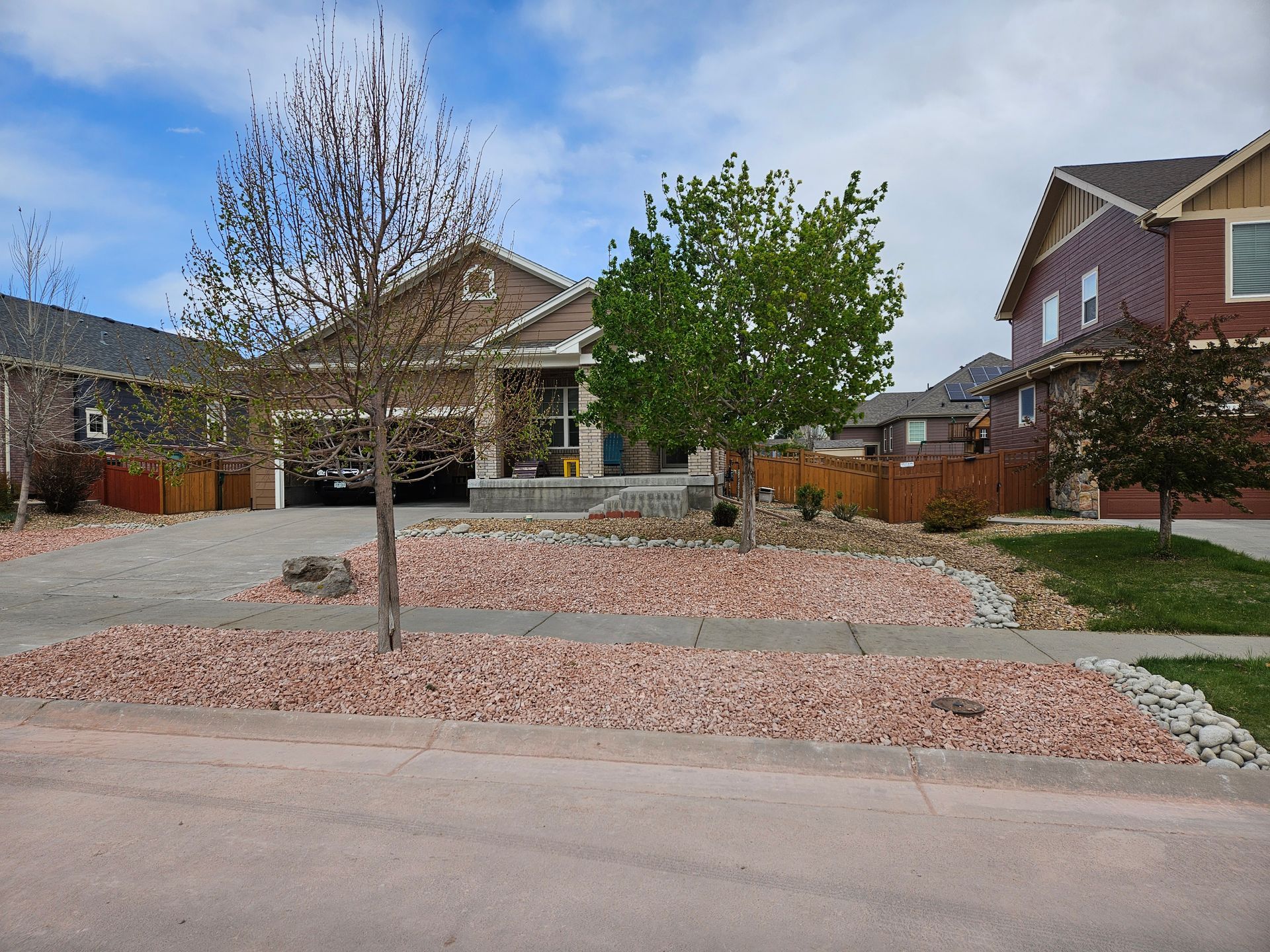 A single-story house with a driveway and reddish-brown rock landscaping, featuring two small trees in the front yard.