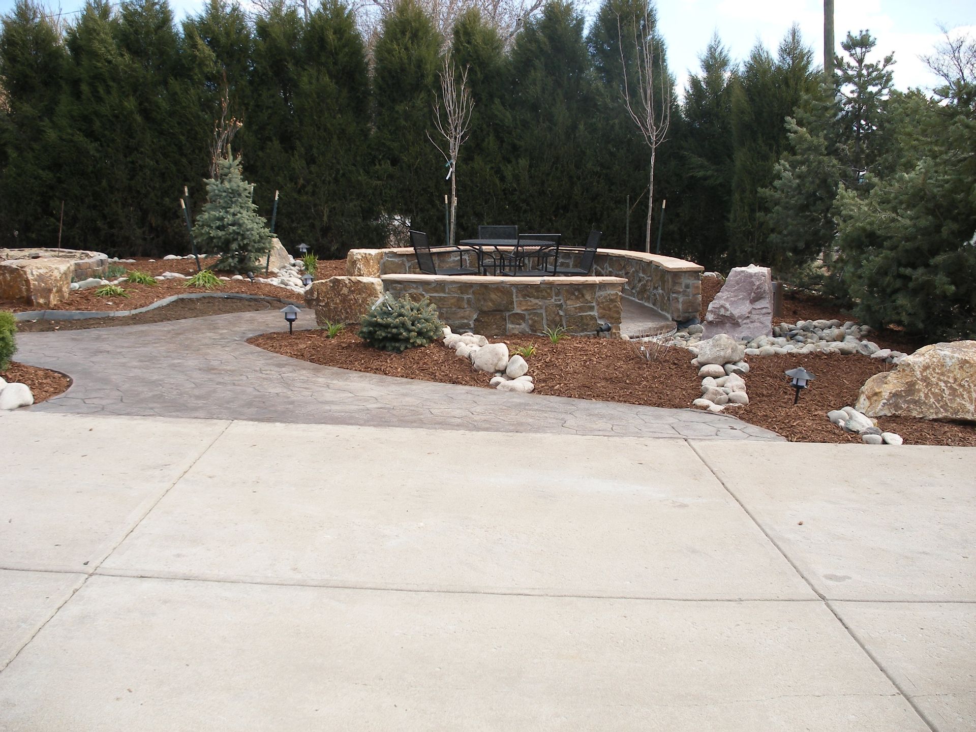 A concrete driveway leads to a patio area with a table and chairs