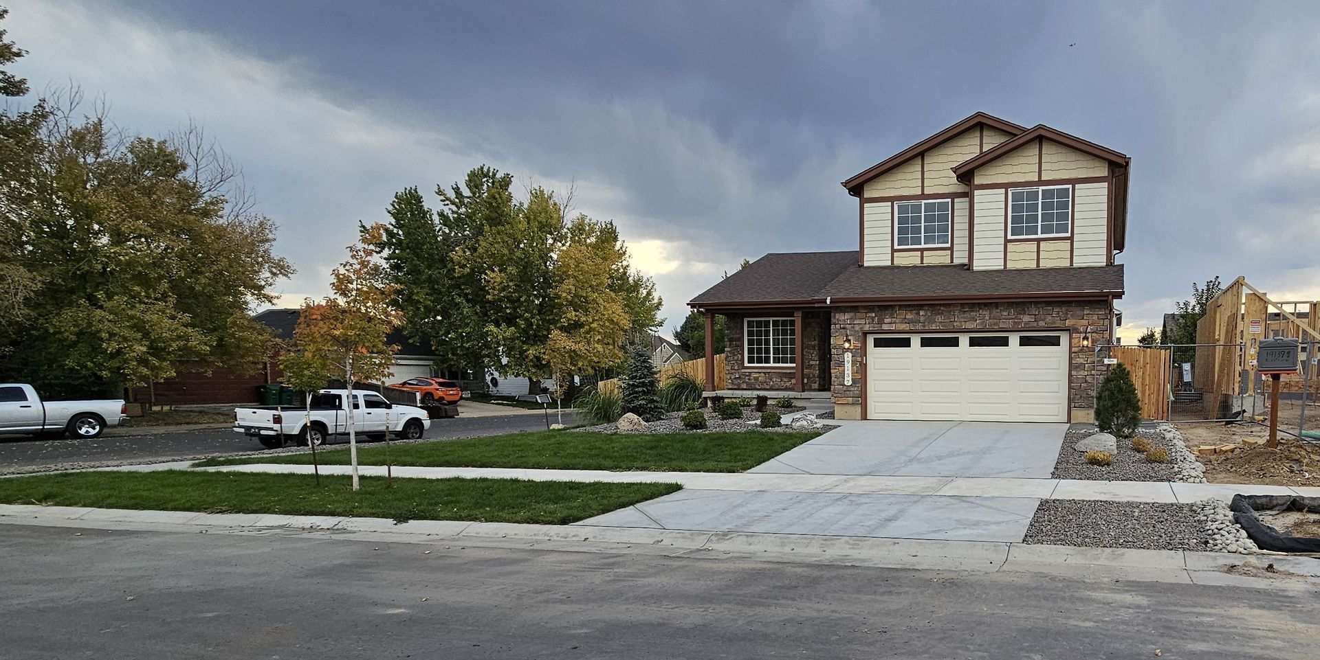 A two-story house with a stone facade and attached garage sits on a street with a cloudy sky in the background.
