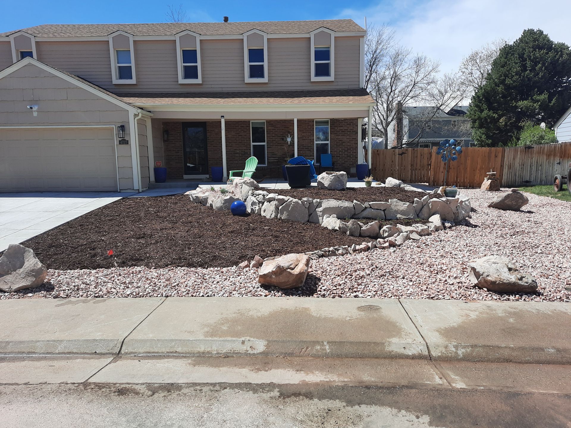 Two-story beige house with a landscaped front yard of gravel, rocks, and mulch.