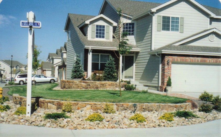 Two-story house with a stone retaining wall, small front yard with manicured lawn and landscaping, and street sign.