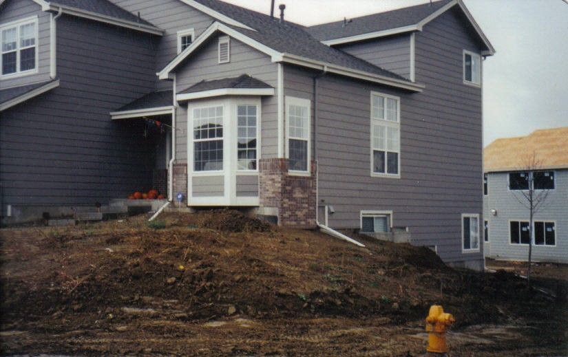 Gray house with bay window and unfinished yard; a yellow fire hydrant is in the foreground.