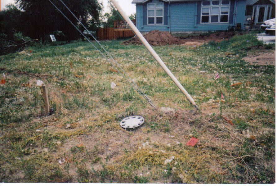 Overgrown grassy lot with a utility pole leaning towards a blue house. A utility access cover sits in the grass.