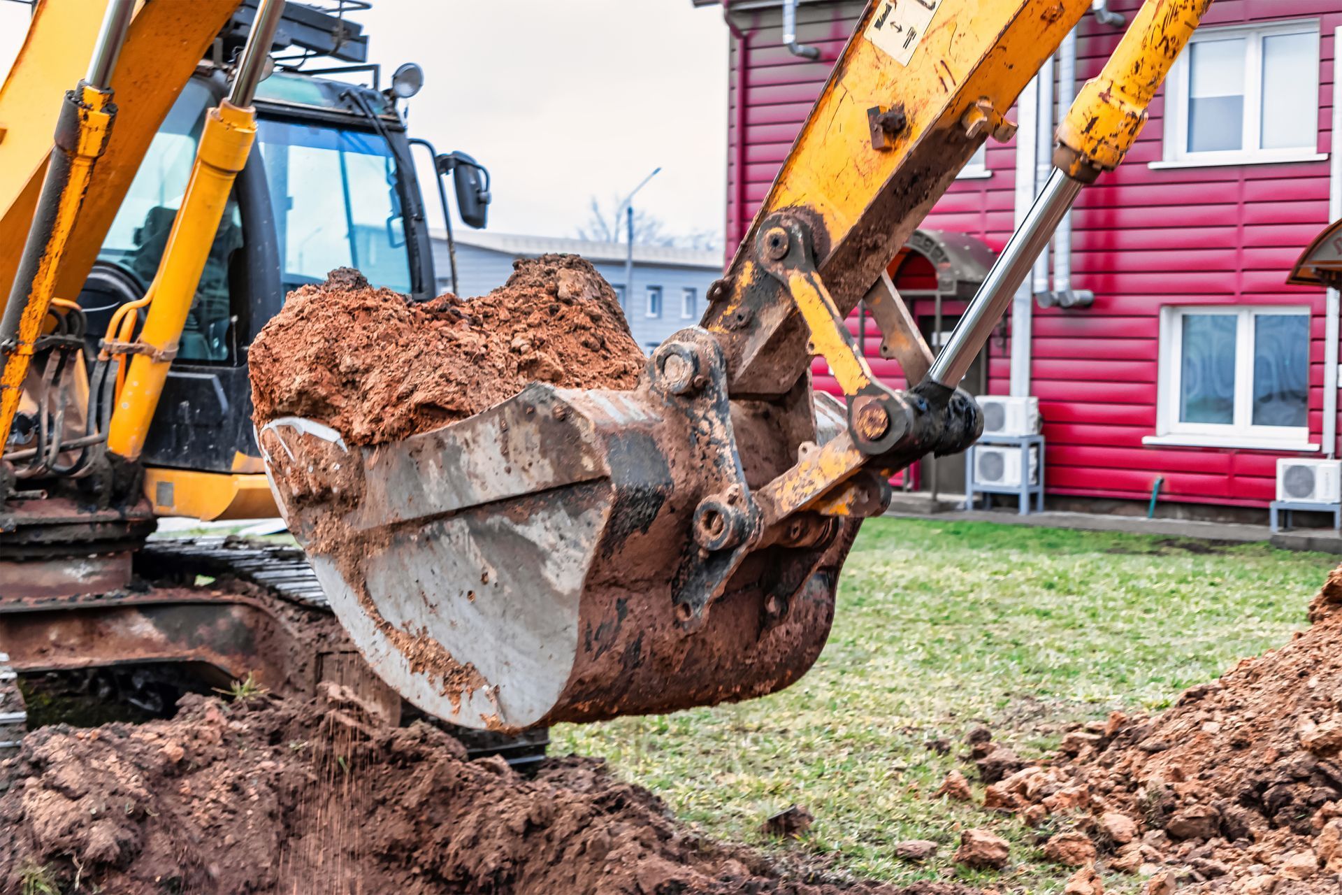 A yellow excavator is digging a hole in front of a red house.