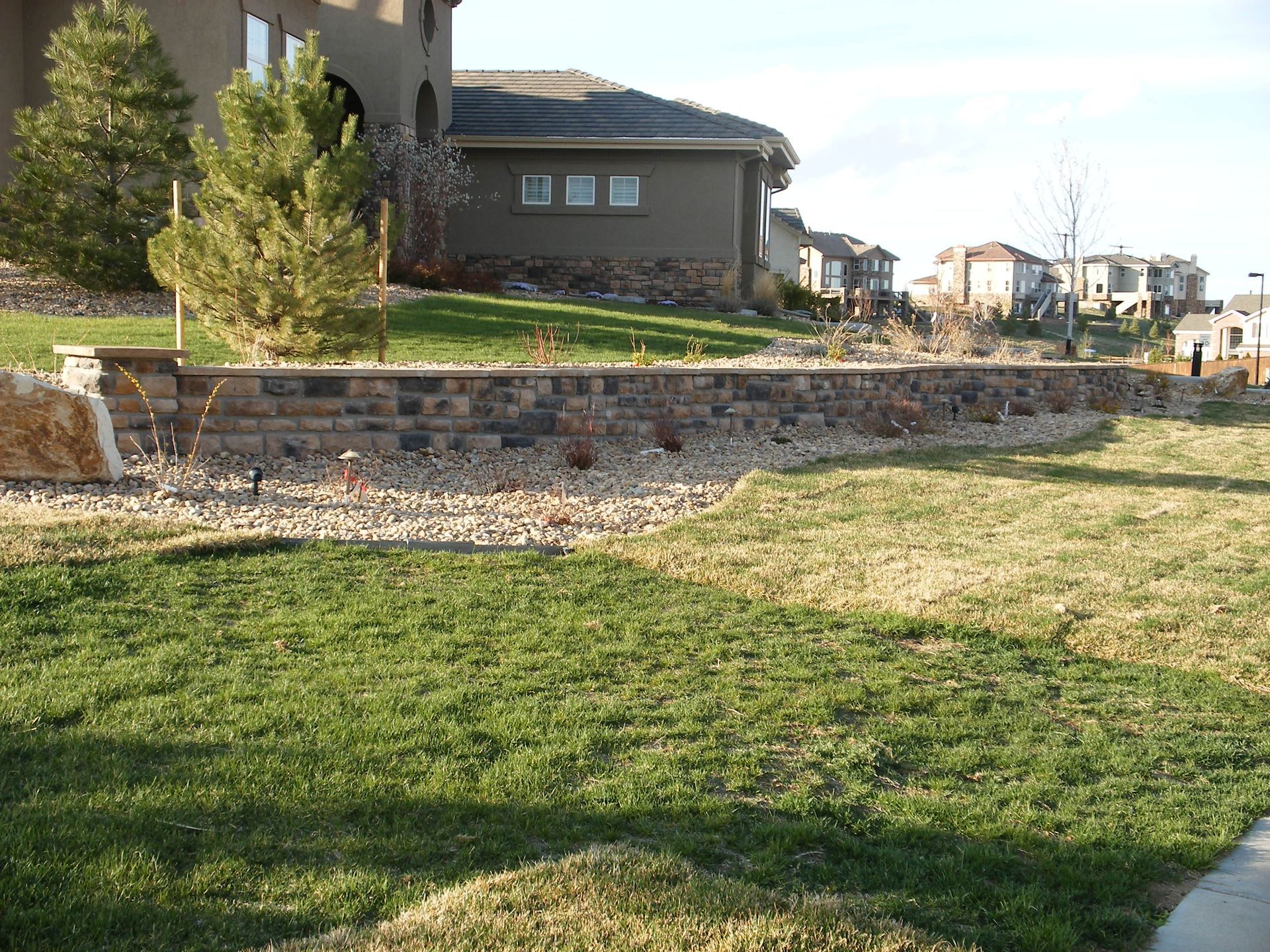 A stone wall surrounds a lush green lawn in front of a house.