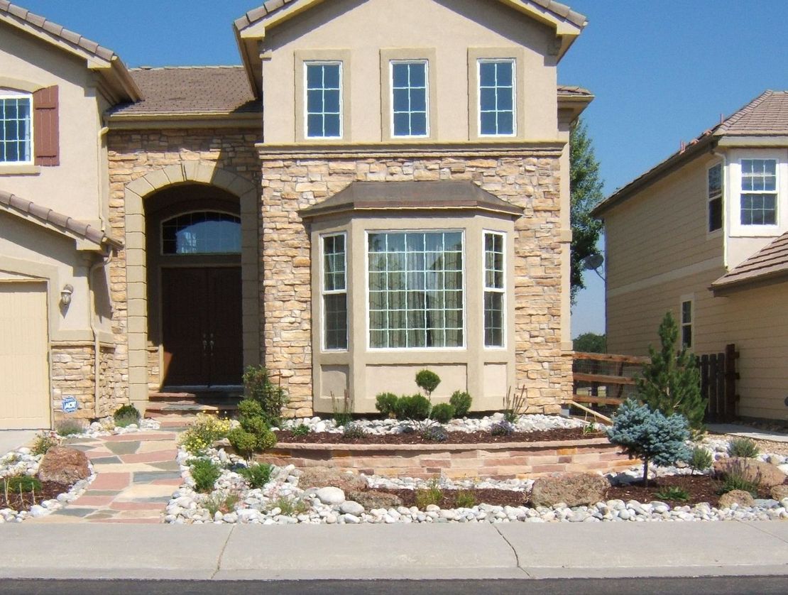 Two-story beige and stone house with a landscaped front yard and bay window.