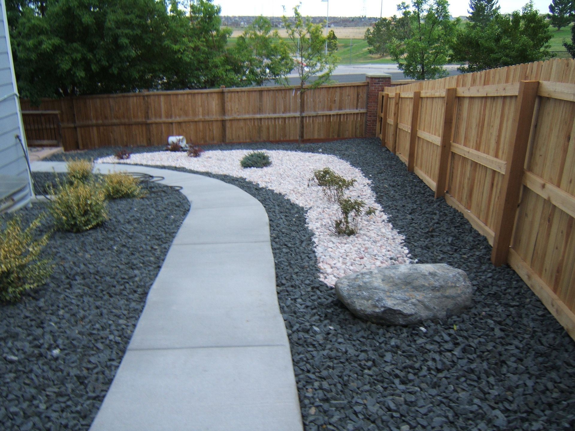 A wooden fence surrounds a concrete walkway in a backyard