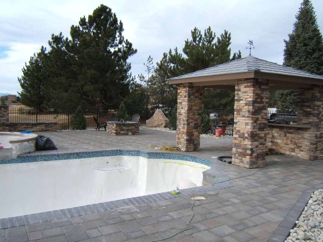 An empty swimming pool with a stone gazebo in the background