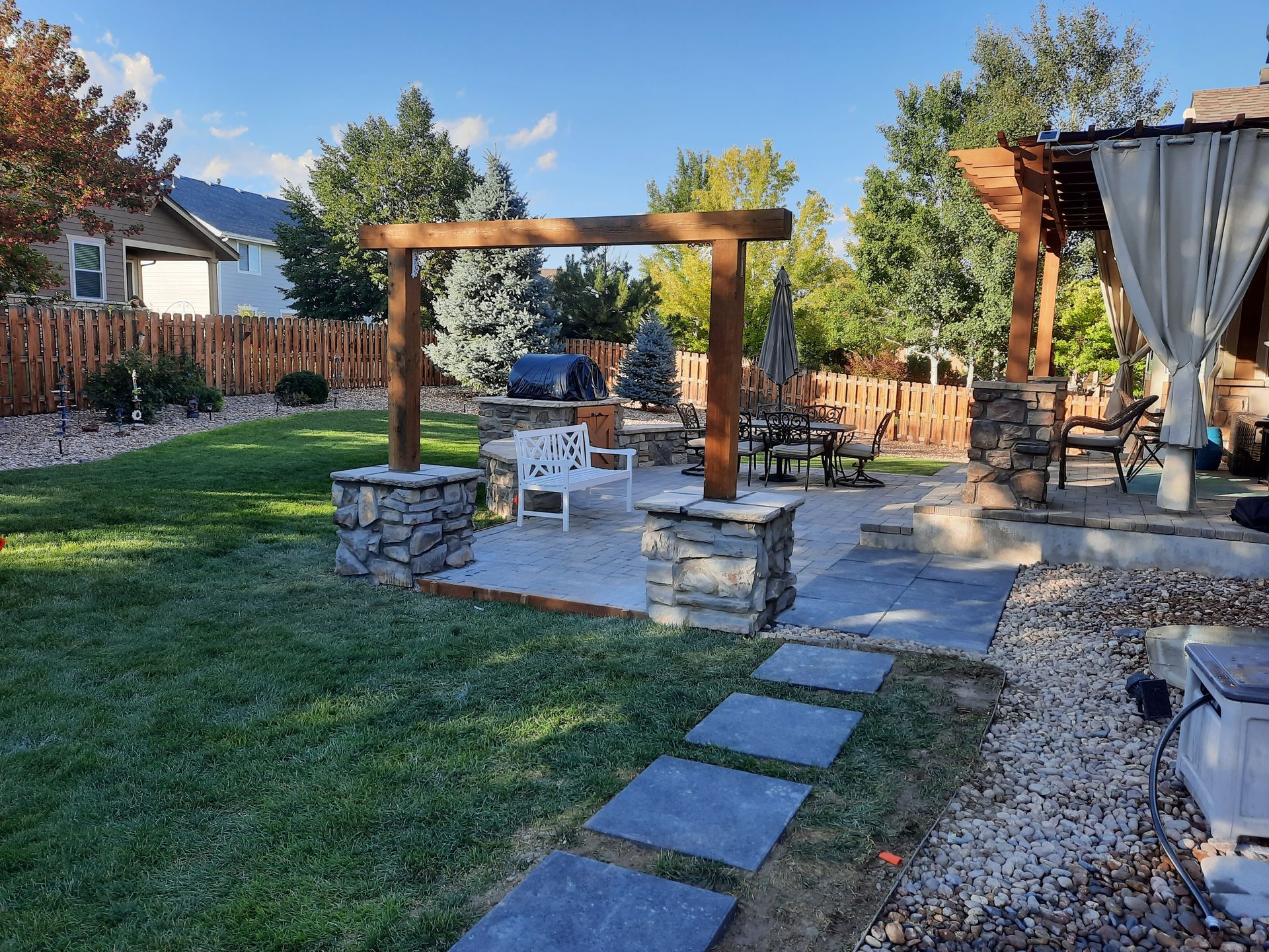 A backyard with a pergola , patio , benches and umbrellas.