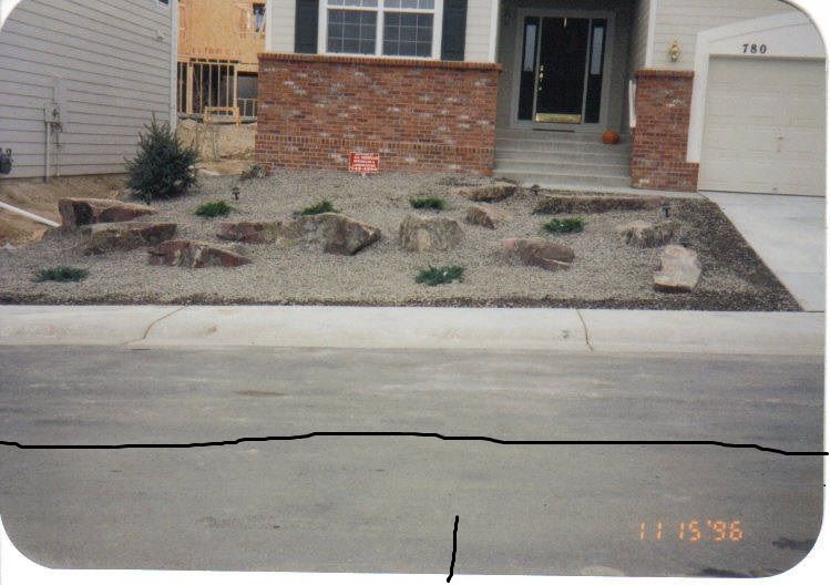 House front with a red brick facade, rock garden, and a gray asphalt street. The date 