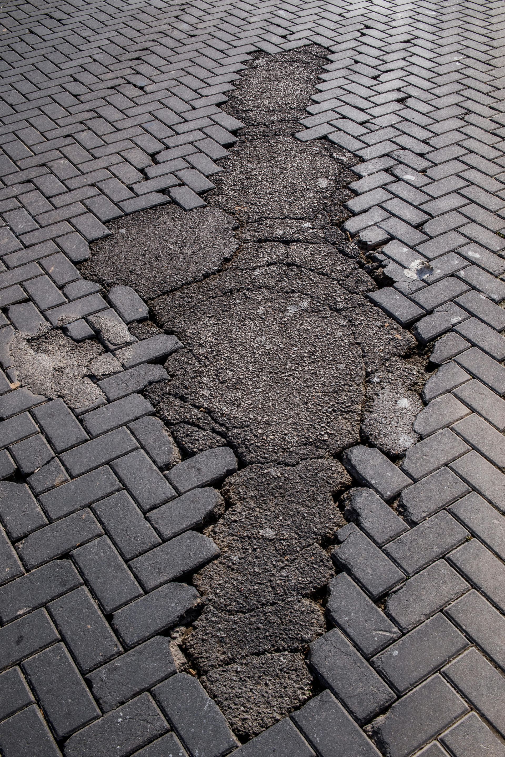 Damaged brick pavement with a large crack exposing asphalt.