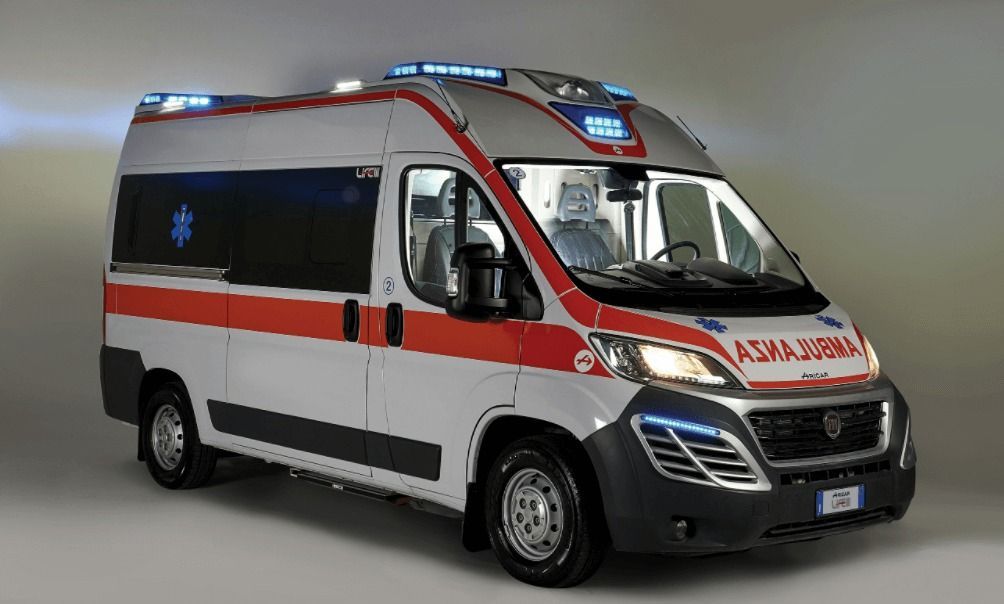 Furgone ambulanza con luci lampeggianti, striscia rossa e stella medica, parcheggiato in uno studio fotografico.