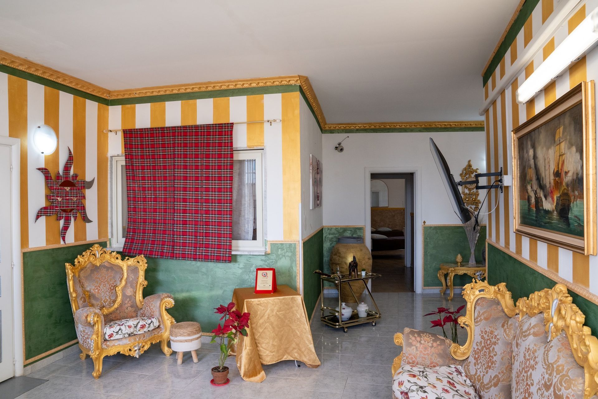 Un soggiorno riccamente decorato con dettagli dorati e verdi, mobili ricercati e una parete a strisce gialle e bianche.