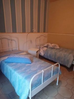 Due letti con struttura in metallo bianco in una stanza con carta da parati a righe blu e bianche. Uno dei letti è dotato di cuscino e coperta blu.