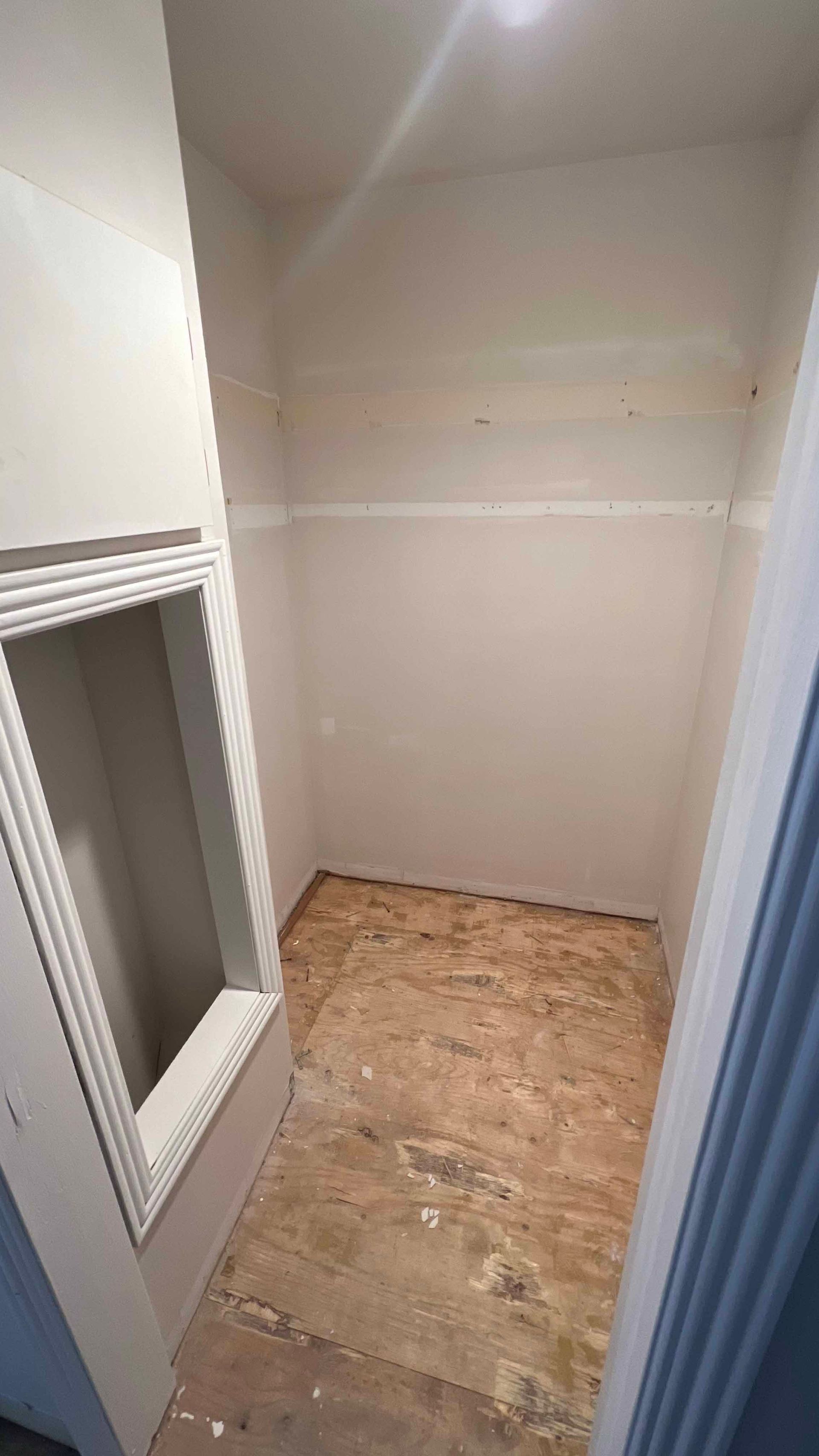 A closet with a window in the wall and a wooden floor.