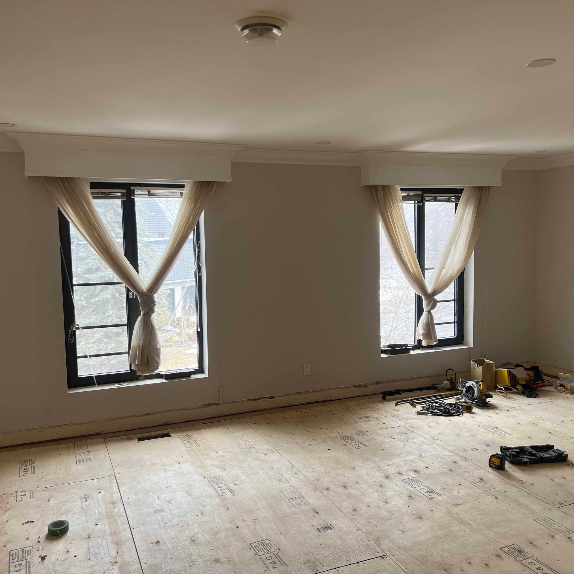 An empty room with two windows and a wooden floor.