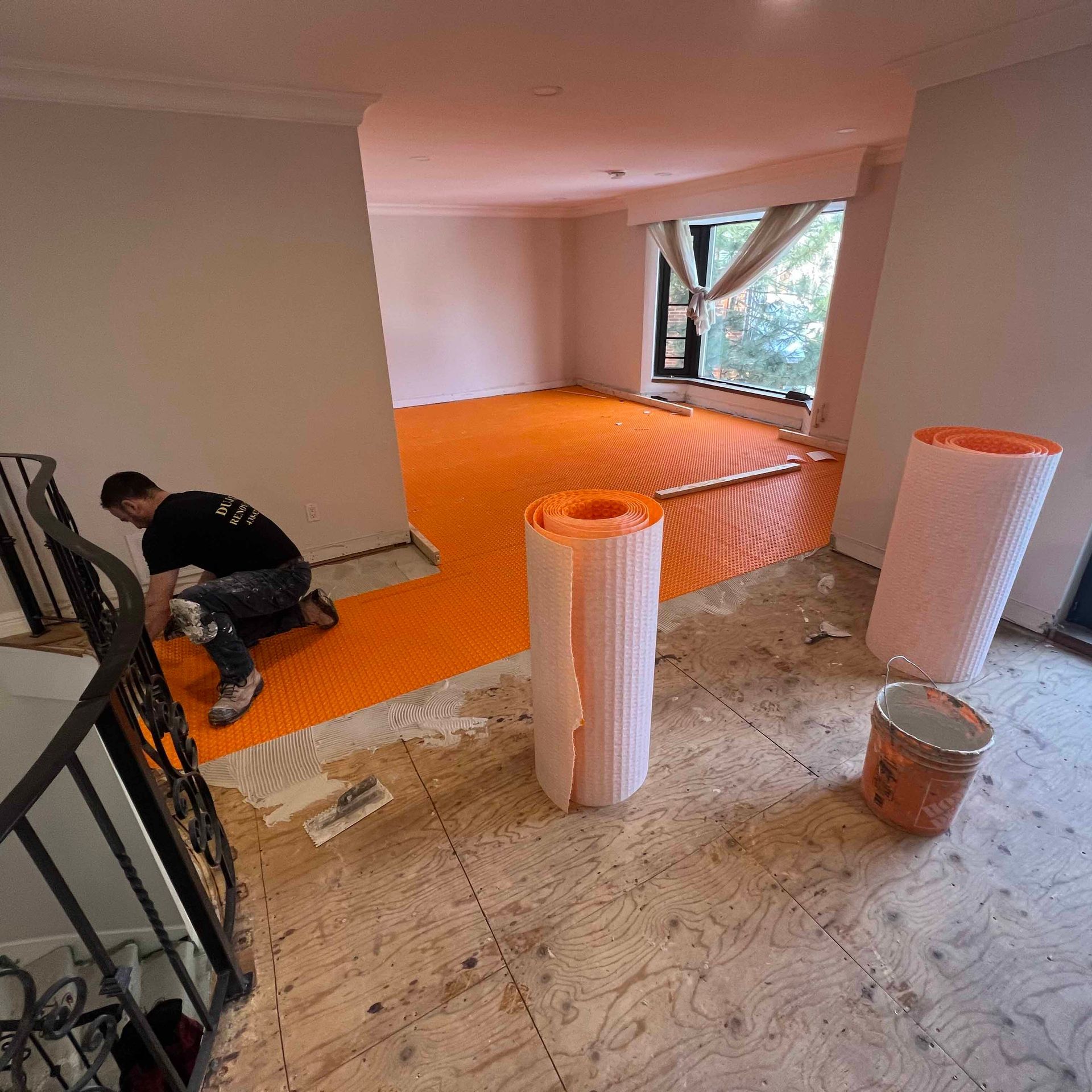 A man is kneeling on the floor in a room with rolls of orange flooring.