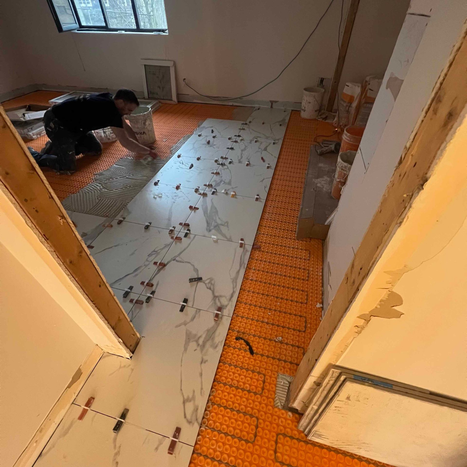 A man is laying tiles on a floor in a room