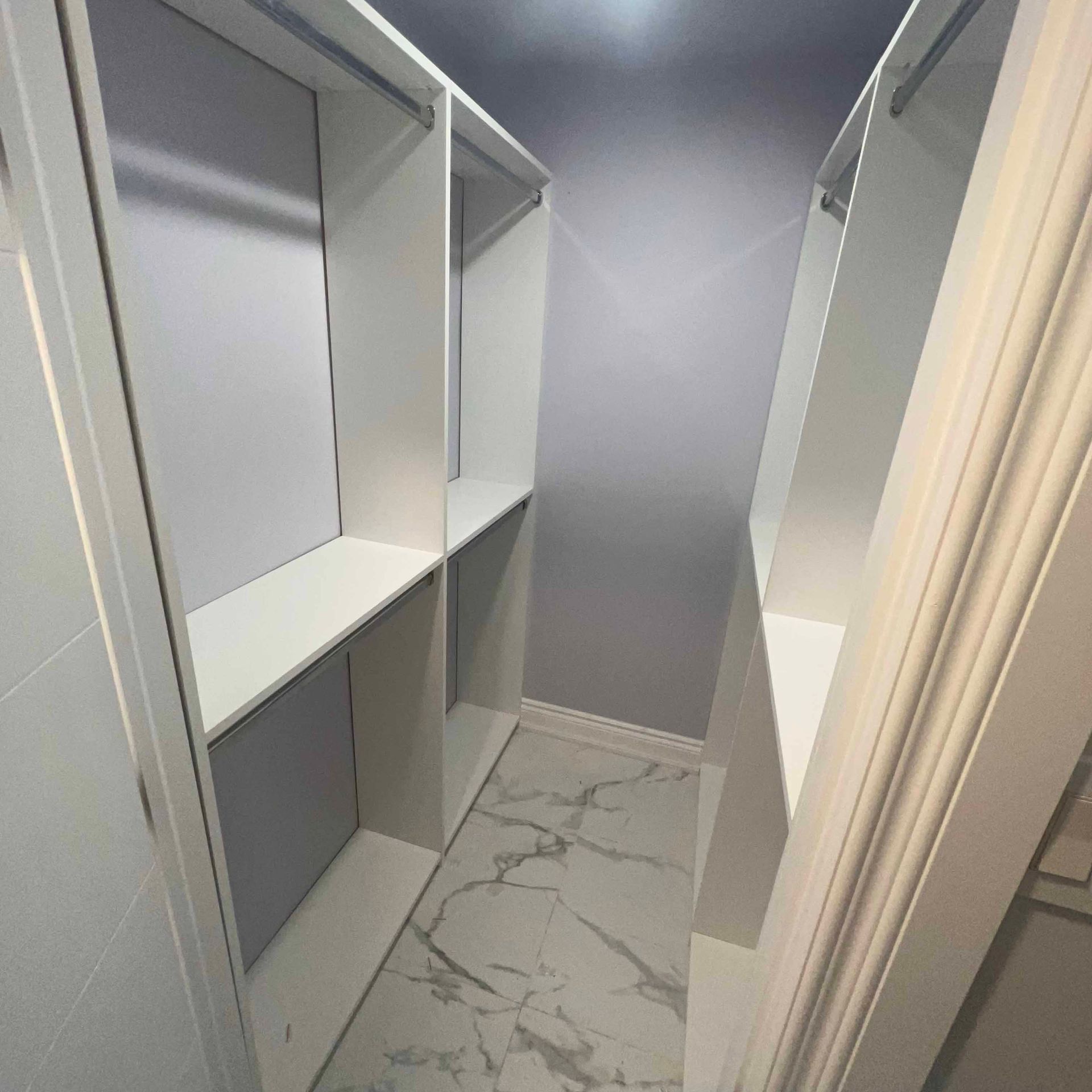 A walk in closet with a marble floor and white shelves