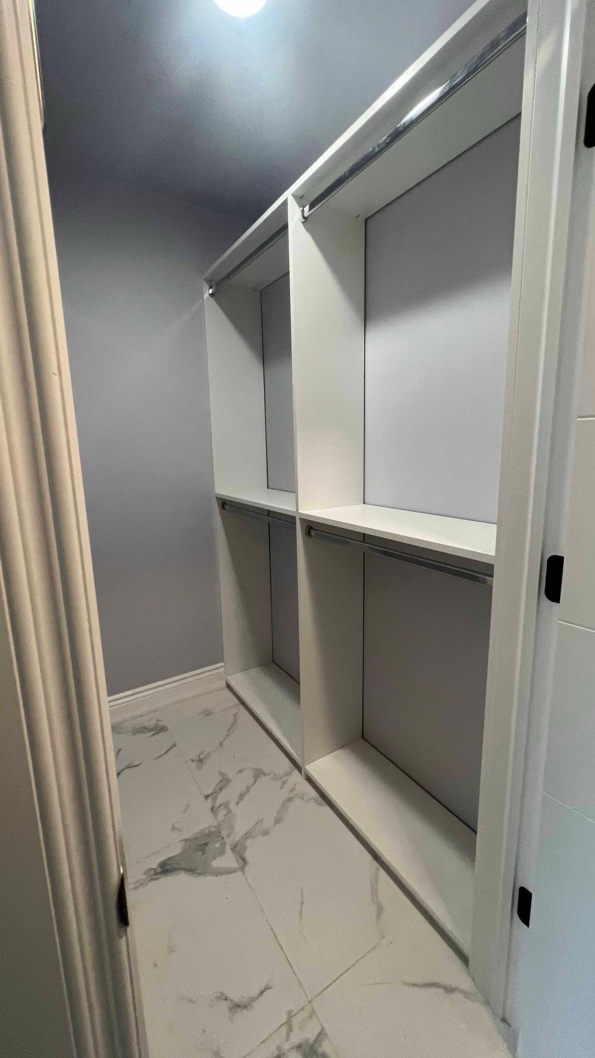 A walk in closet with a marble floor and white shelves.