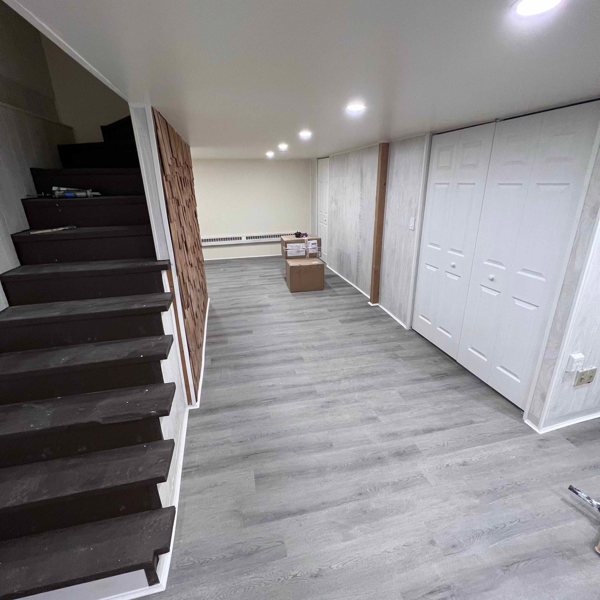 Basement interior with stairs, gray wood flooring, white doors, and recessed lighting.