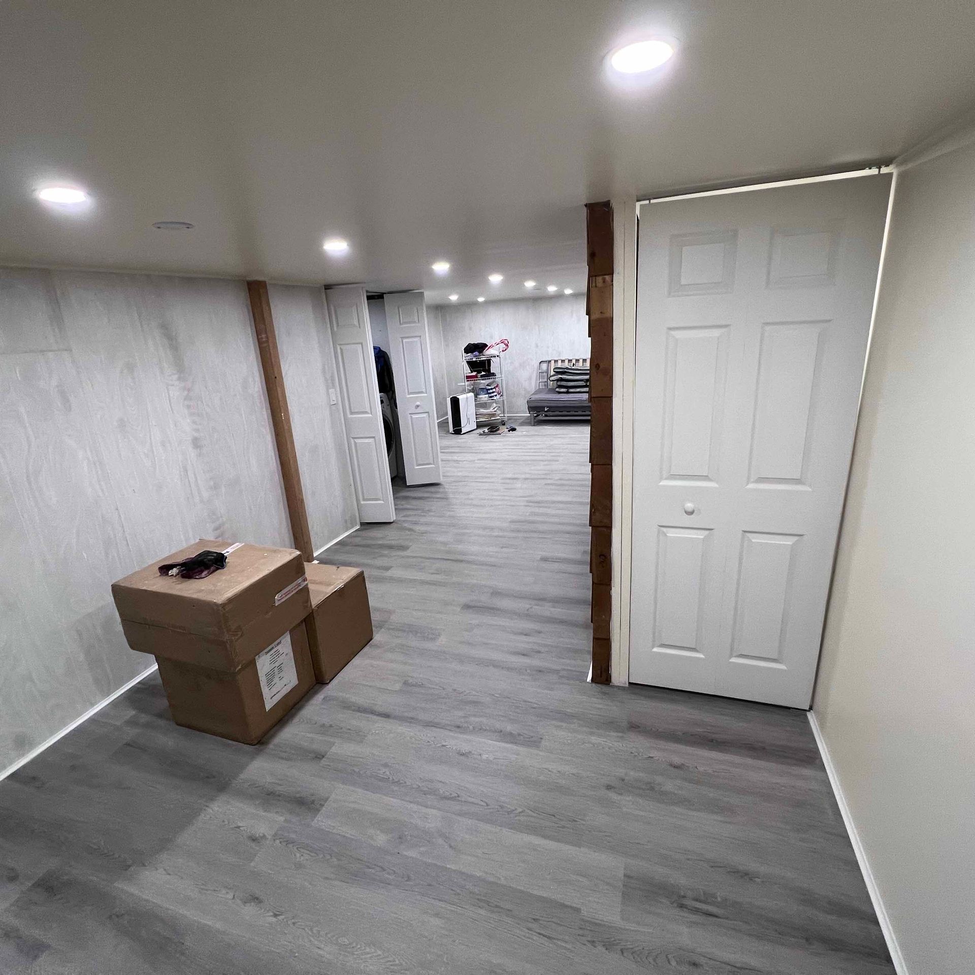 A hallway in a basement with boxes on the floor and a door.