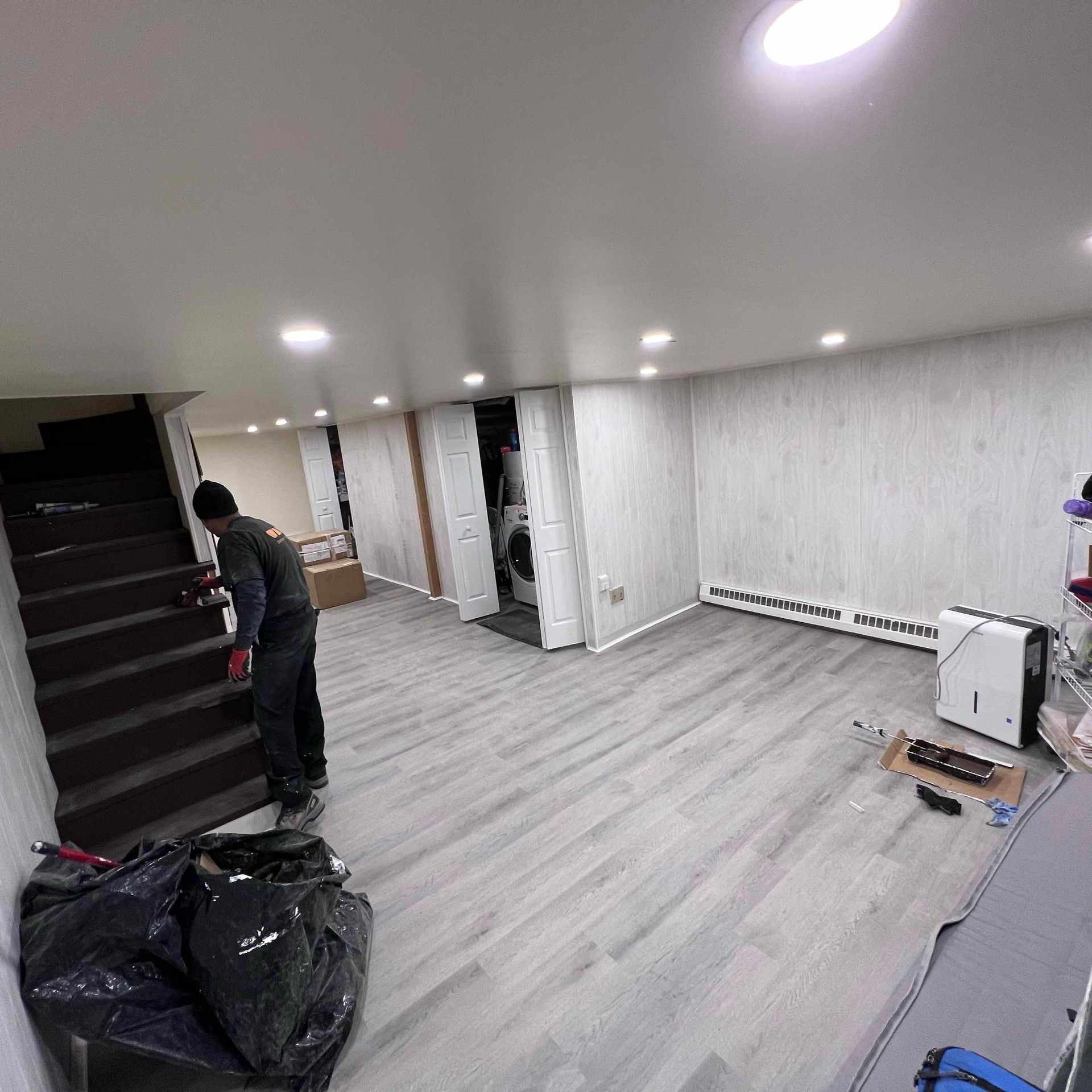 A man is standing in a basement with wooden floors and stairs.