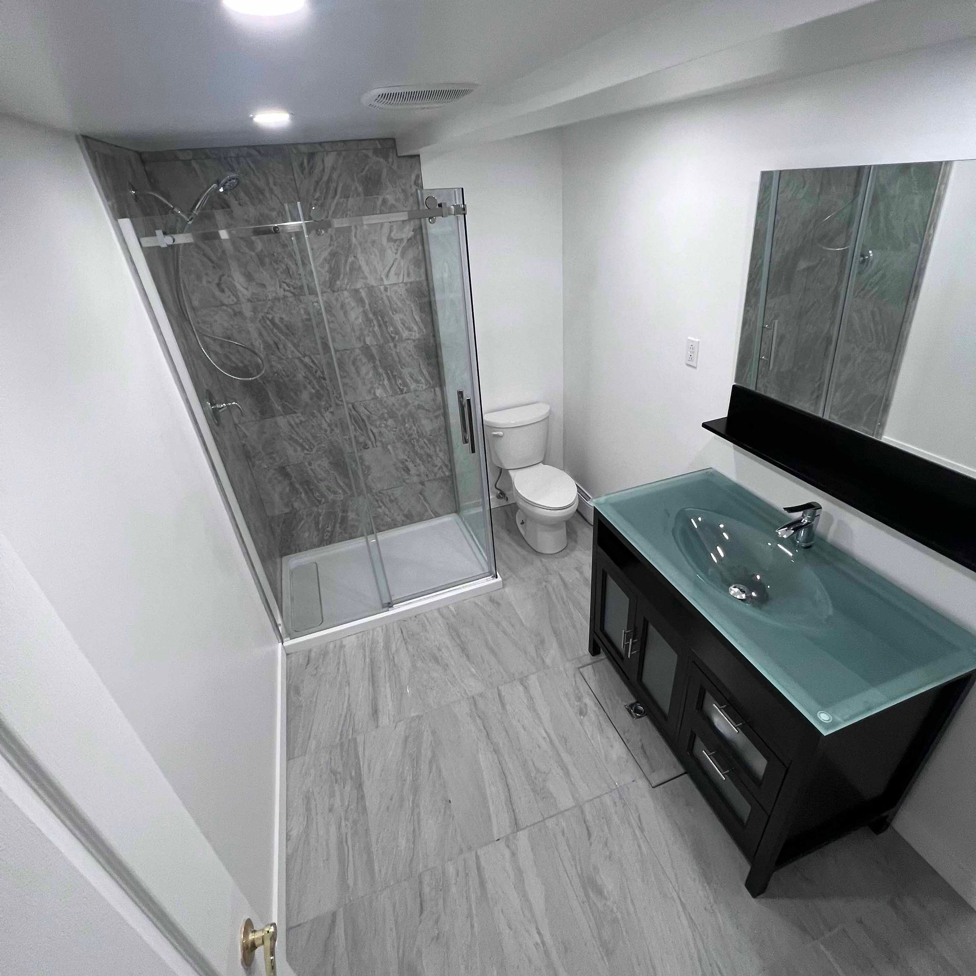 Bathroom with gray tile, glass shower, black vanity, and white toilet.
