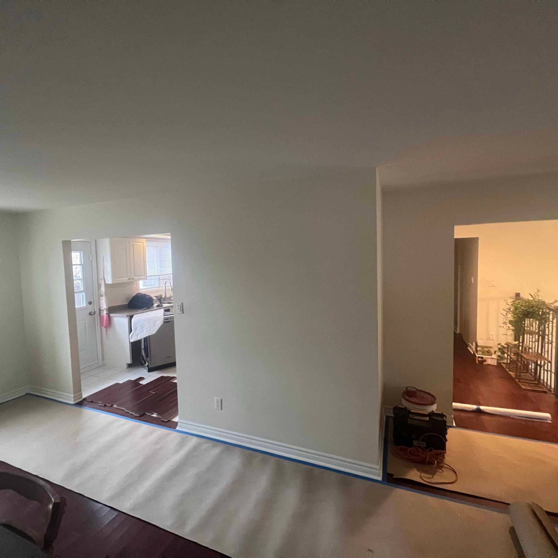 A living room with white walls and hardwood floors is being painted.