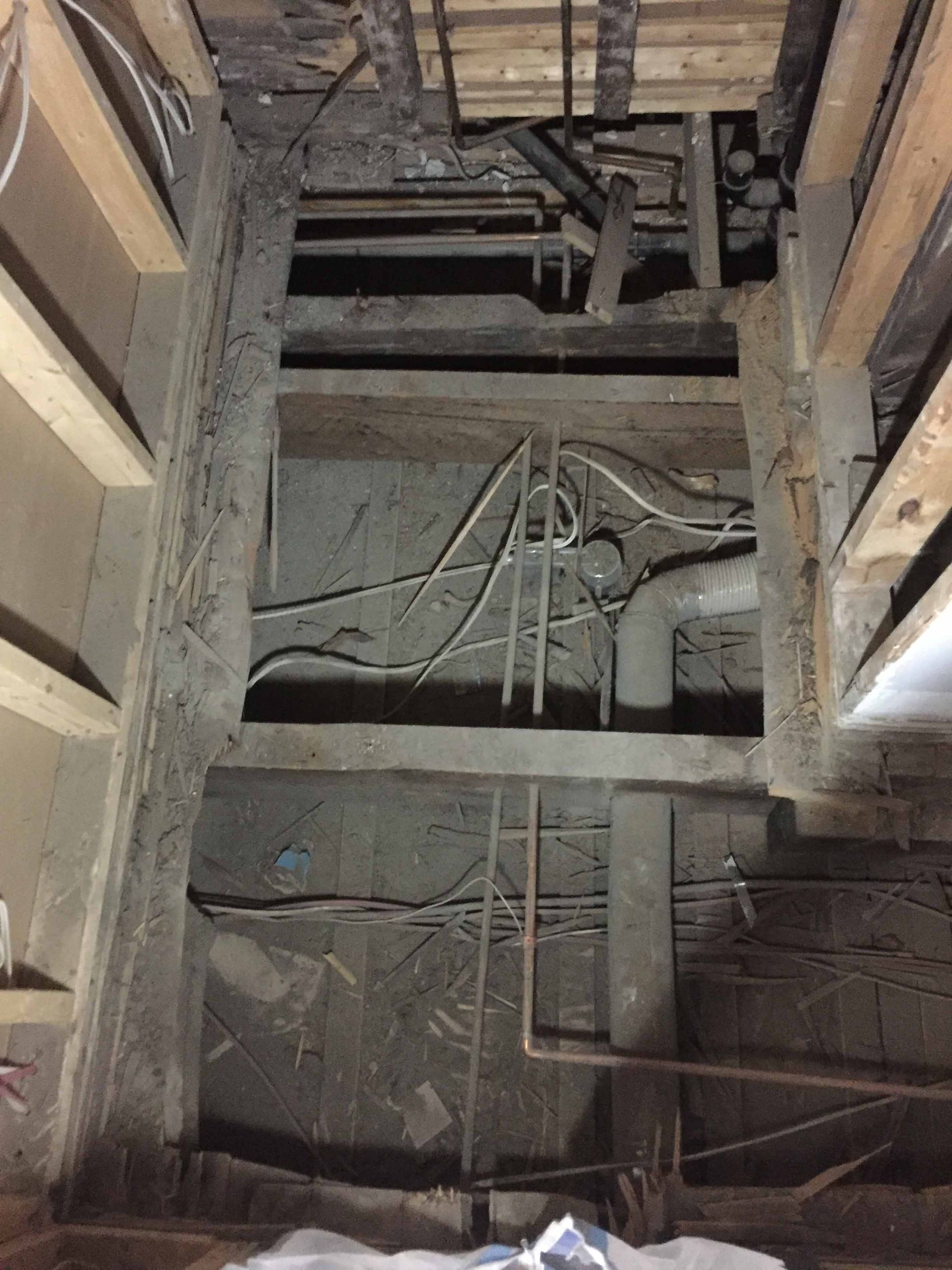 Looking up at the ceiling of a building with pipes and wires.