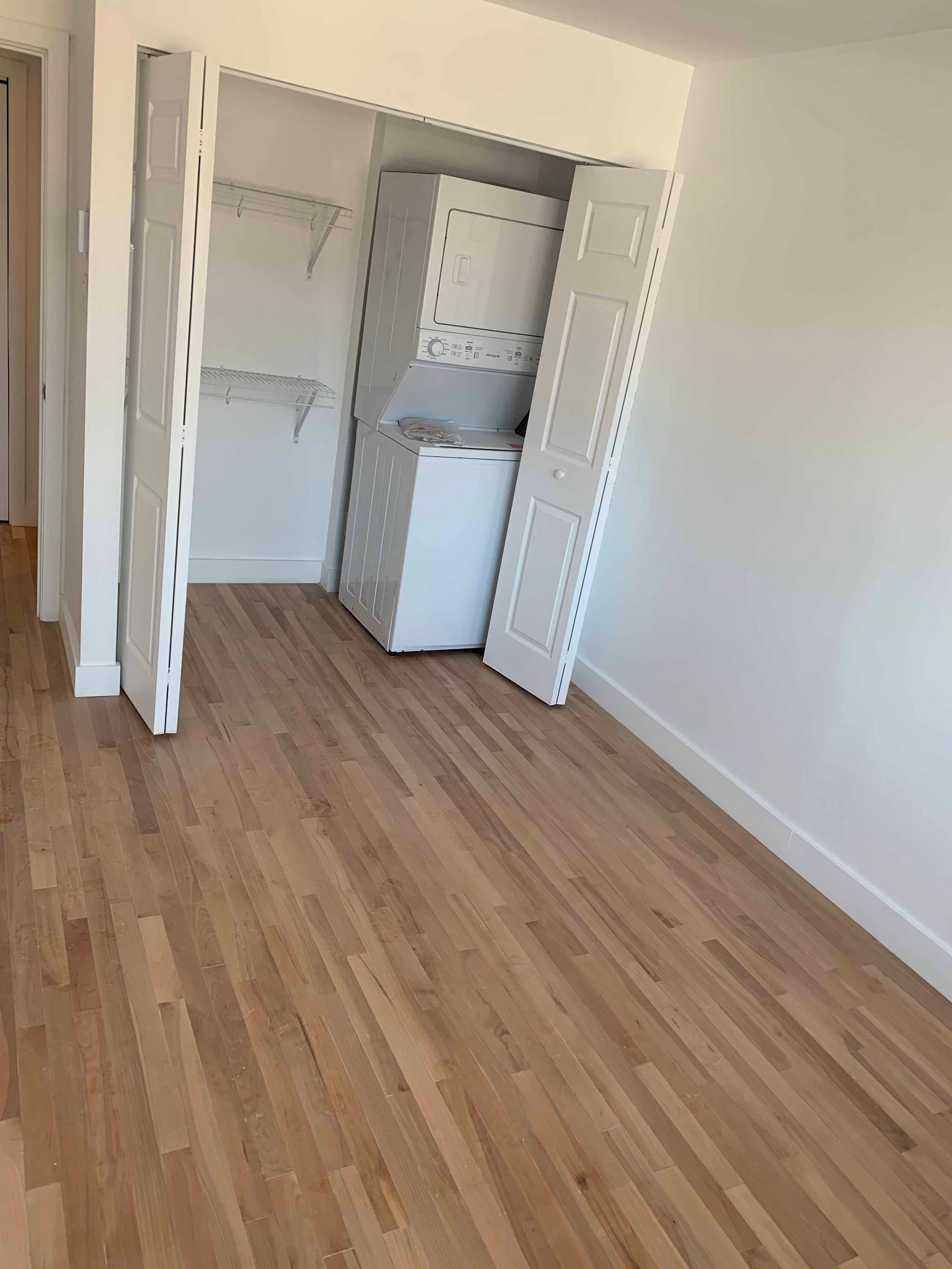 An empty room with hardwood floors and a washer and dryer in a closet.