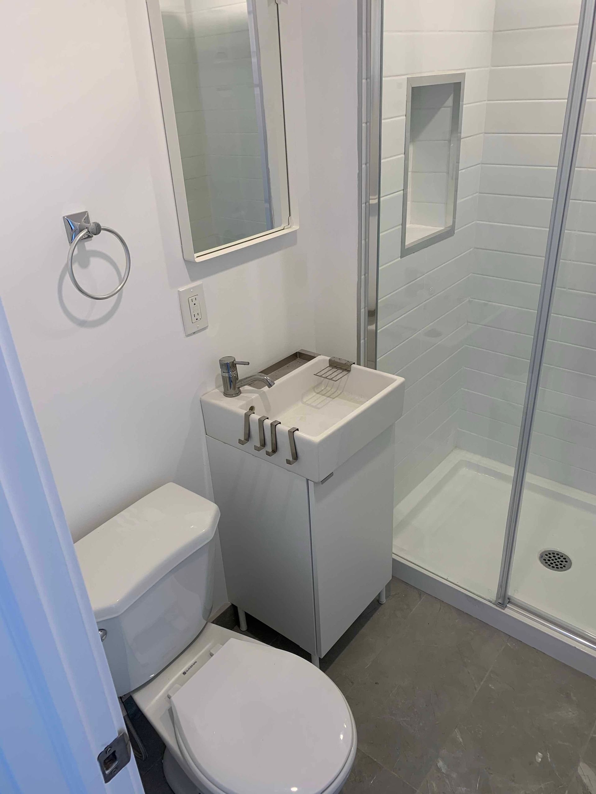 Small white bathroom with toilet, sink, shower, and mirror.