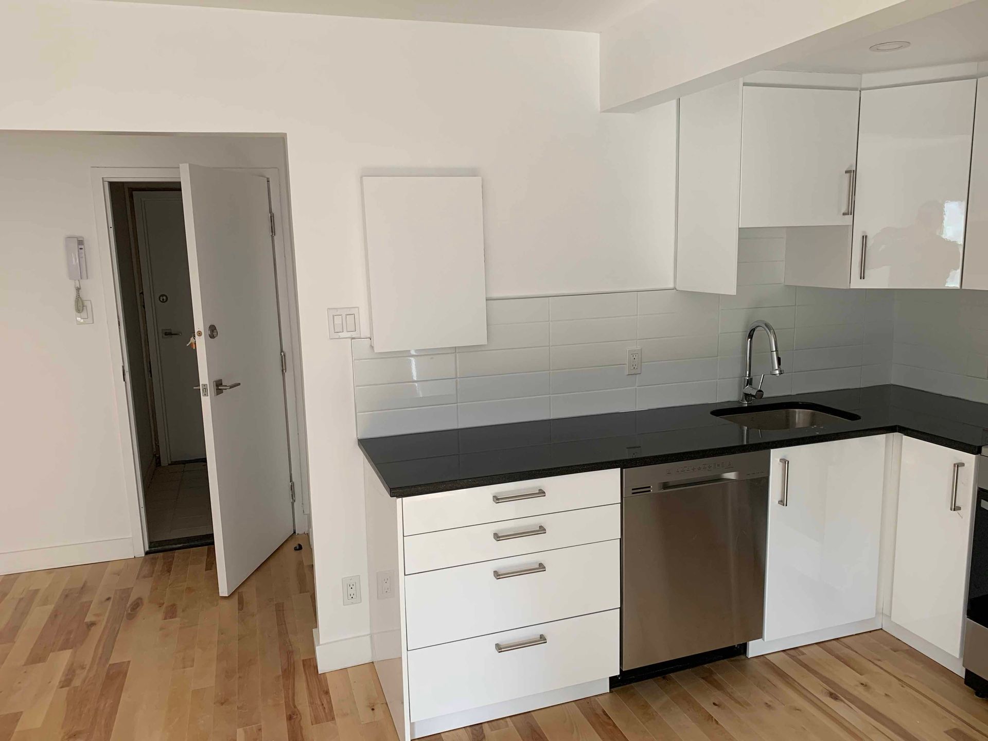 Modern kitchen with white cabinets, black countertop, stainless steel appliances, and hardwood floors.