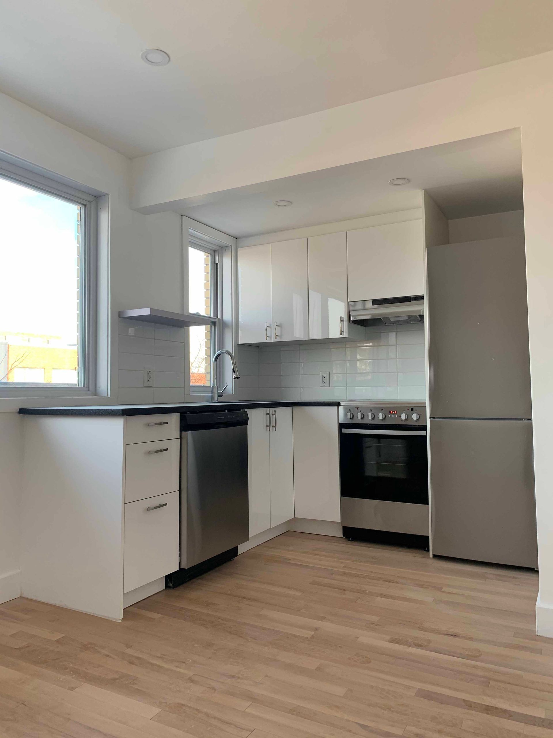 White kitchen with stainless steel appliances and light wood floors.