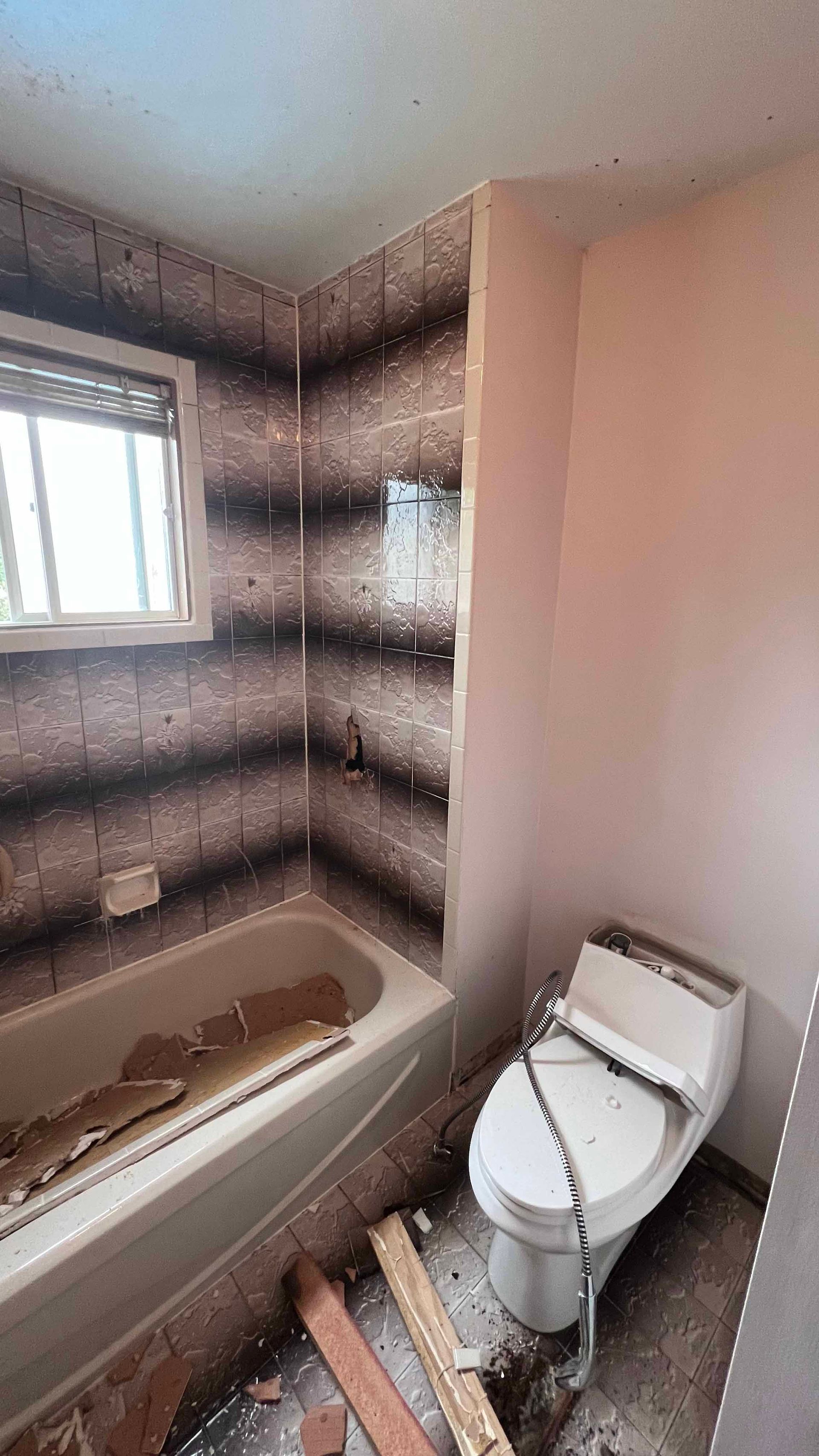 A bathroom with a toilet , bathtub and window.