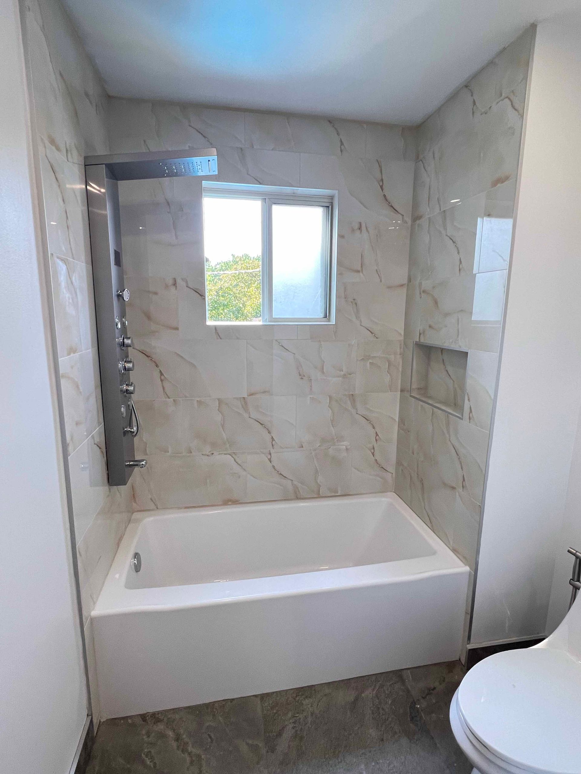 A bathroom with a tub , toilet , shower and window.