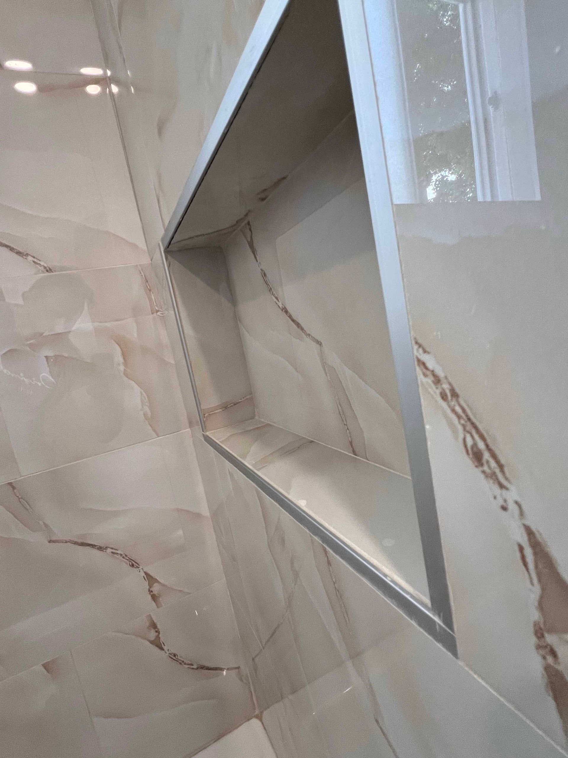 A bathroom with a stainless steel shelf in the wall.