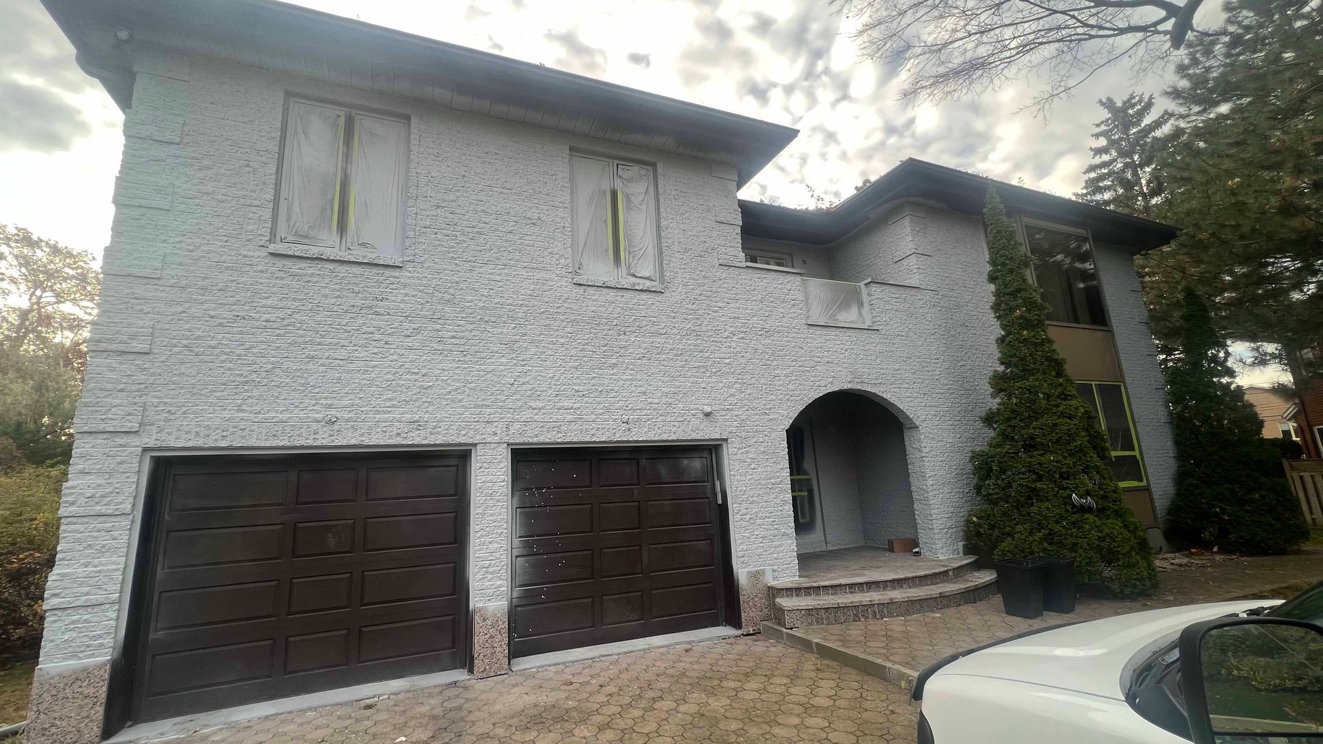 A large white brick house with two garage doors and a car parked in front of it.
