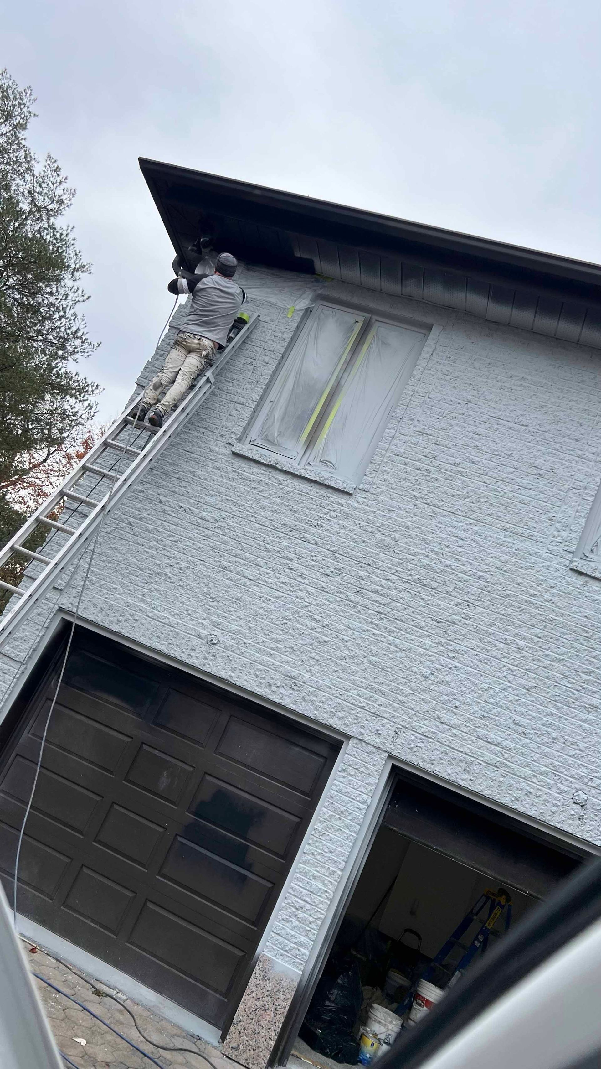 A man is standing on a ladder on the side of a house.