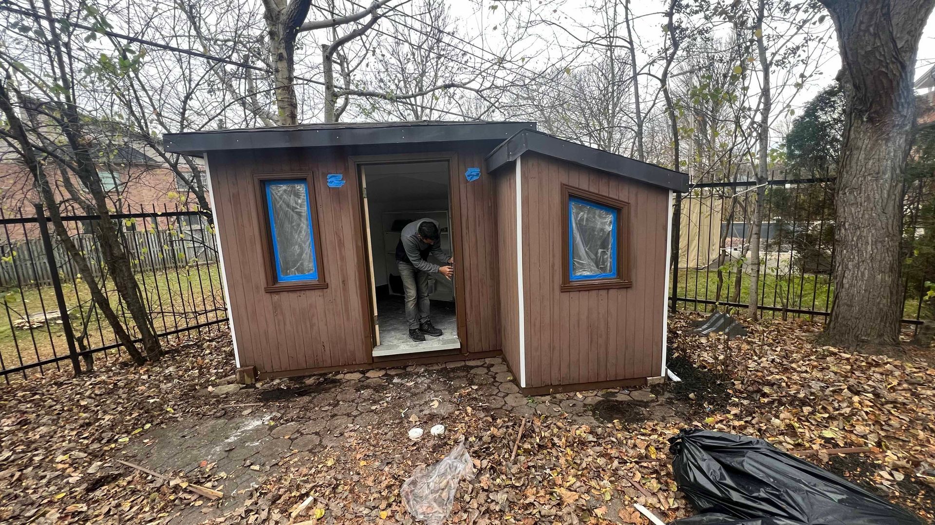 A man is working on a small wooden shed in the backyard.