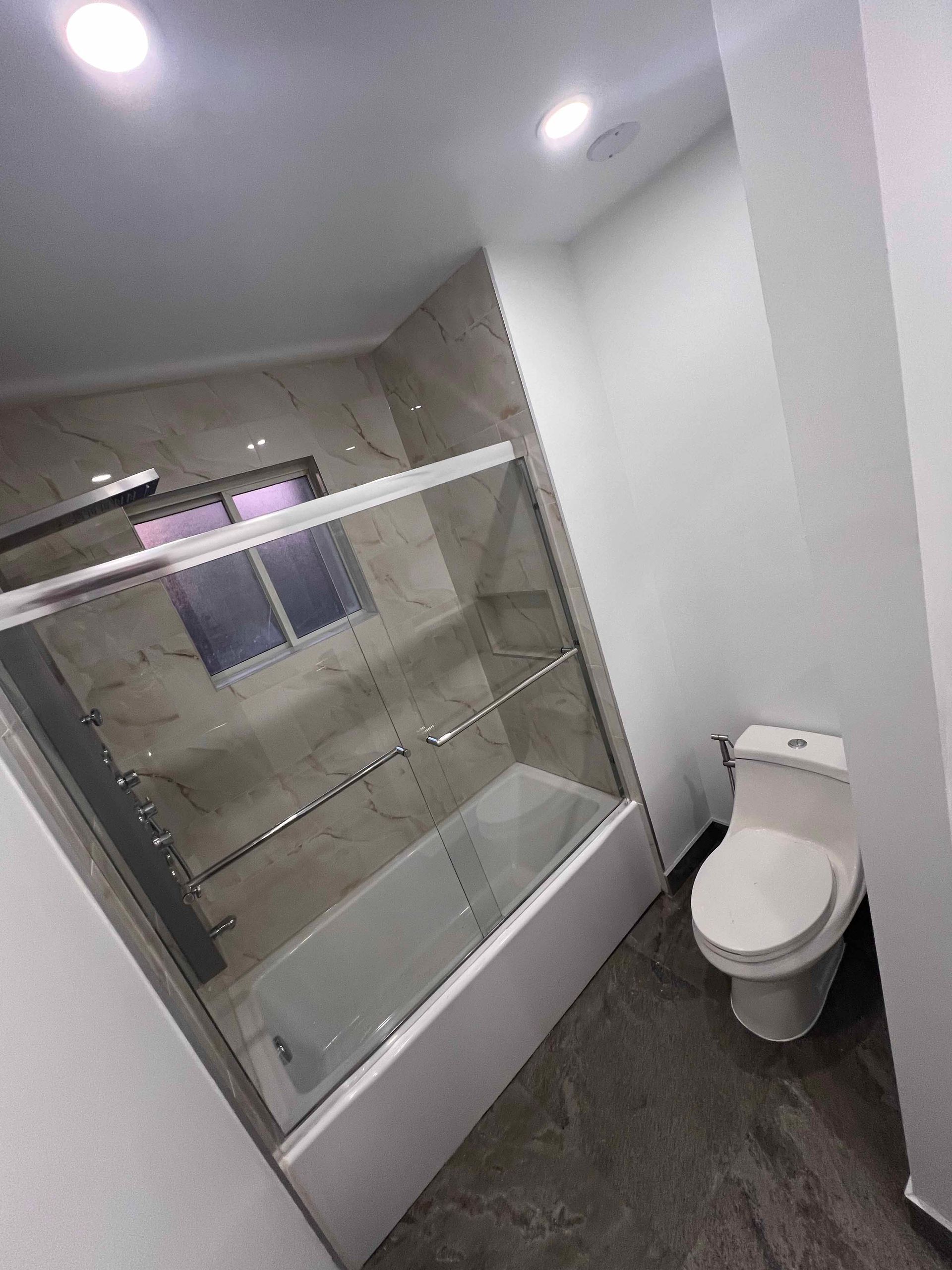 A bathroom with a toilet , tub , shower and window.